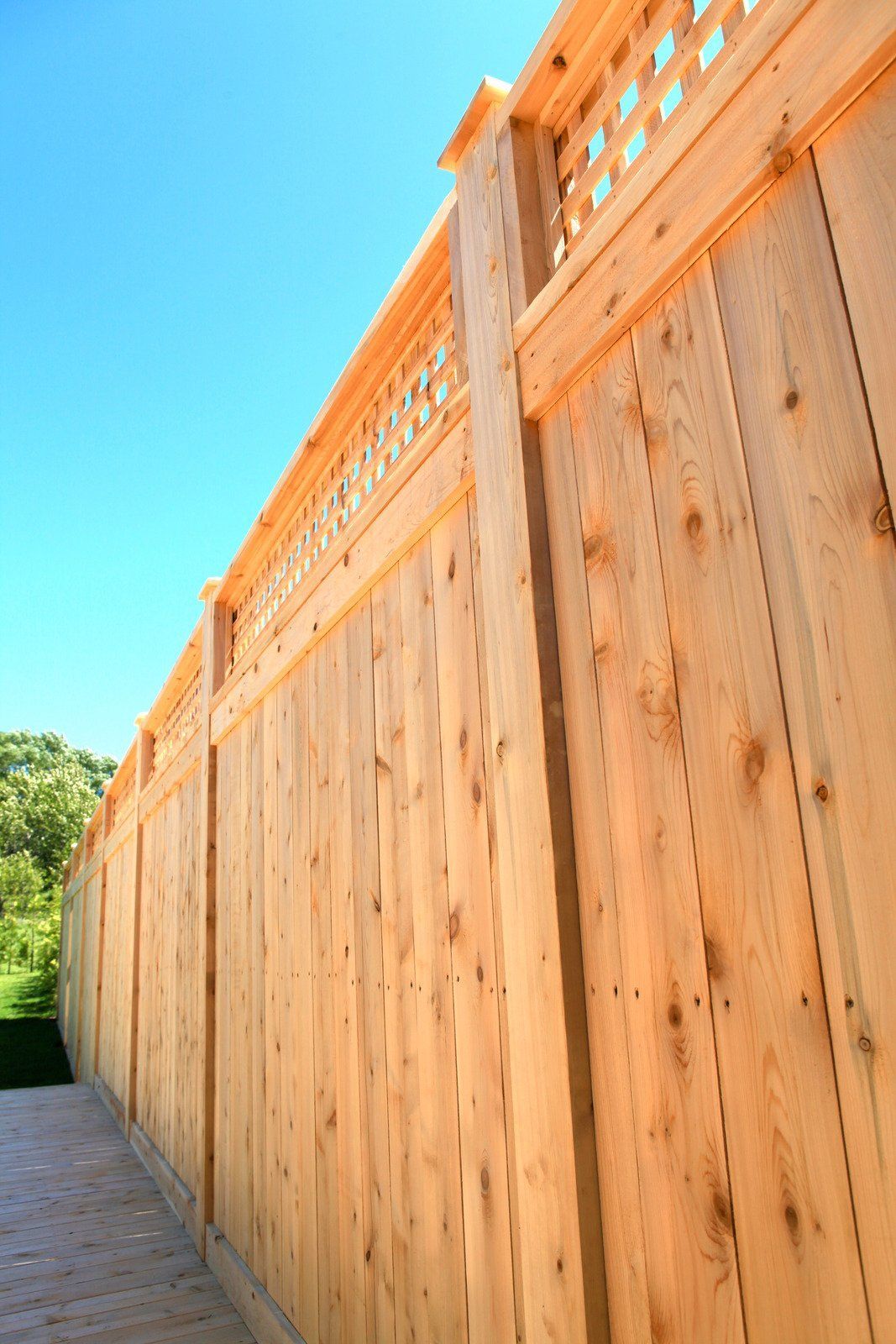 Wooden privacy fence with lattice top under a blue sky.