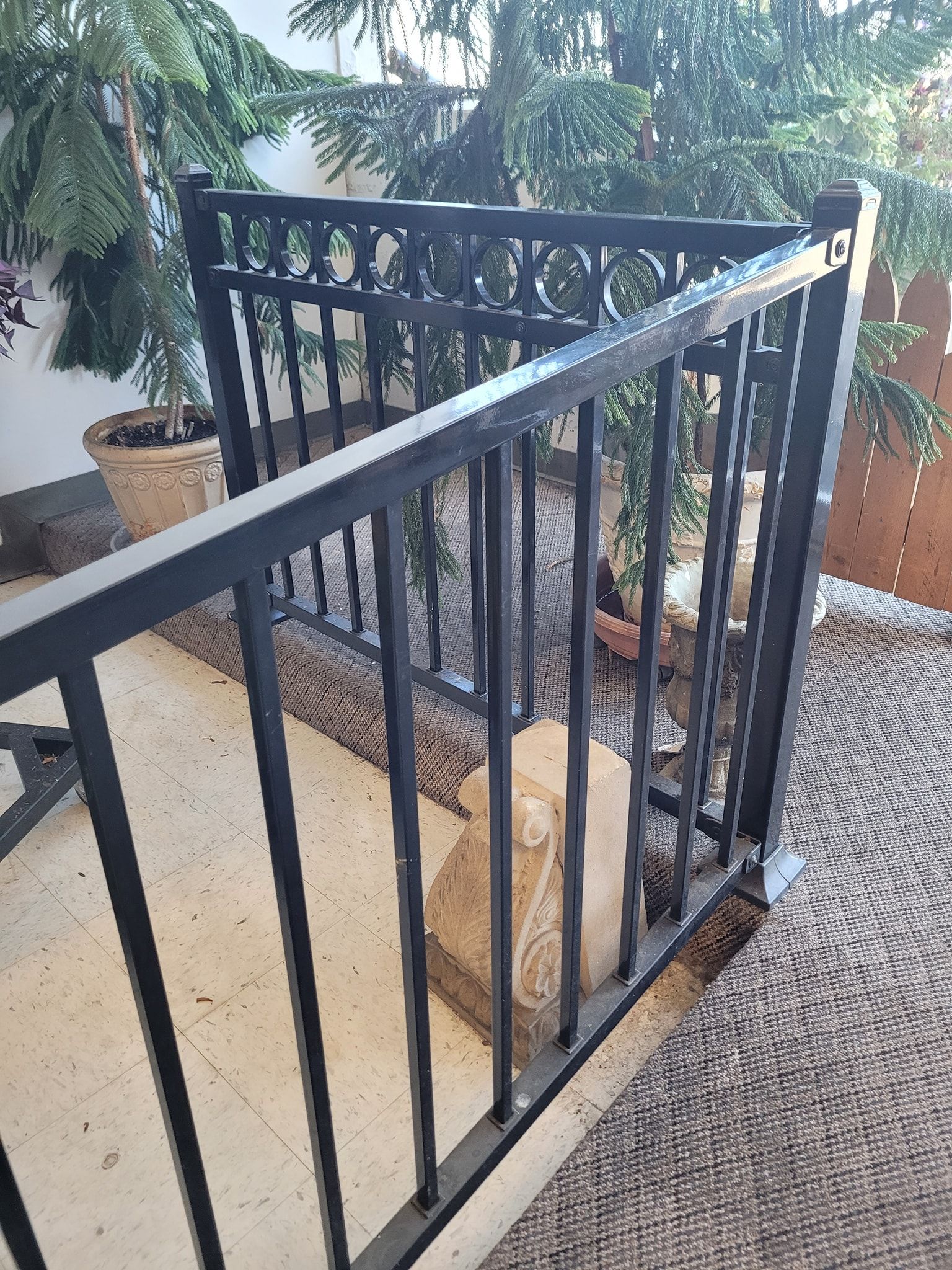 Black metal railing on a patio, with a rug and potted plants in the background.