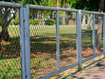 Chain-link fence topped with razor wire against a blue sky with clouds.