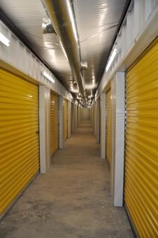 A long, narrow indoor hallway lined with closed, yellow roll-up storage unit doors under bright overhead lighting.