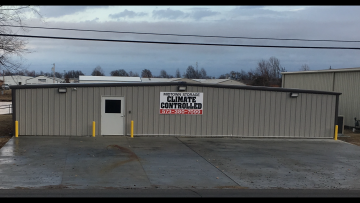 A gray, metal commercial storage building with a central white door and a sign reading