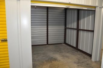 An empty, indoor self-storage unit with grey corrugated metal walls and a concrete floor.