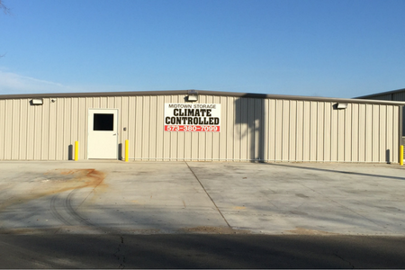 A light beige, metal-sided storage building with a single door and a sign reading 