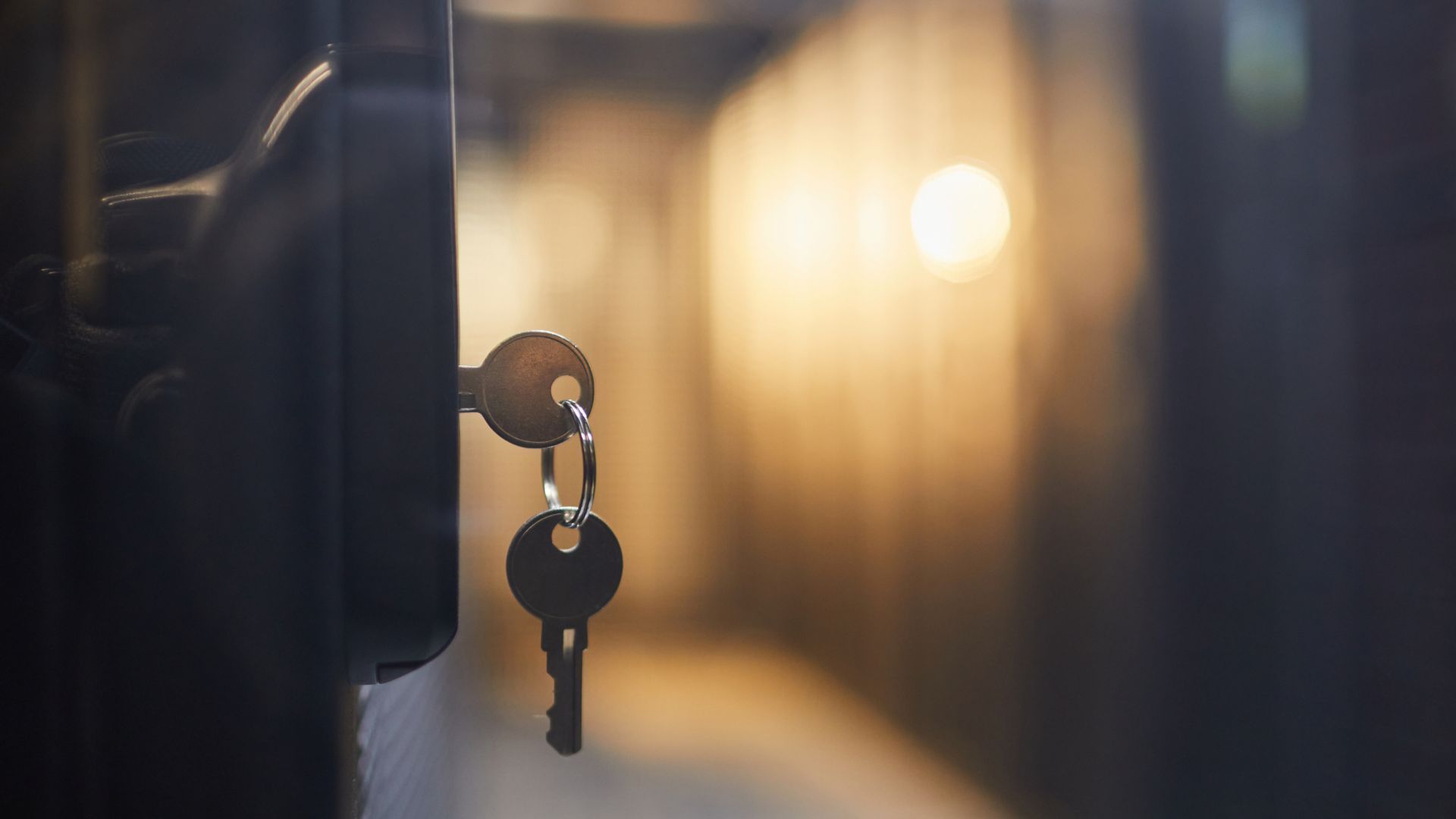 A pair of keys with one in a door in a fairly dark corridor.