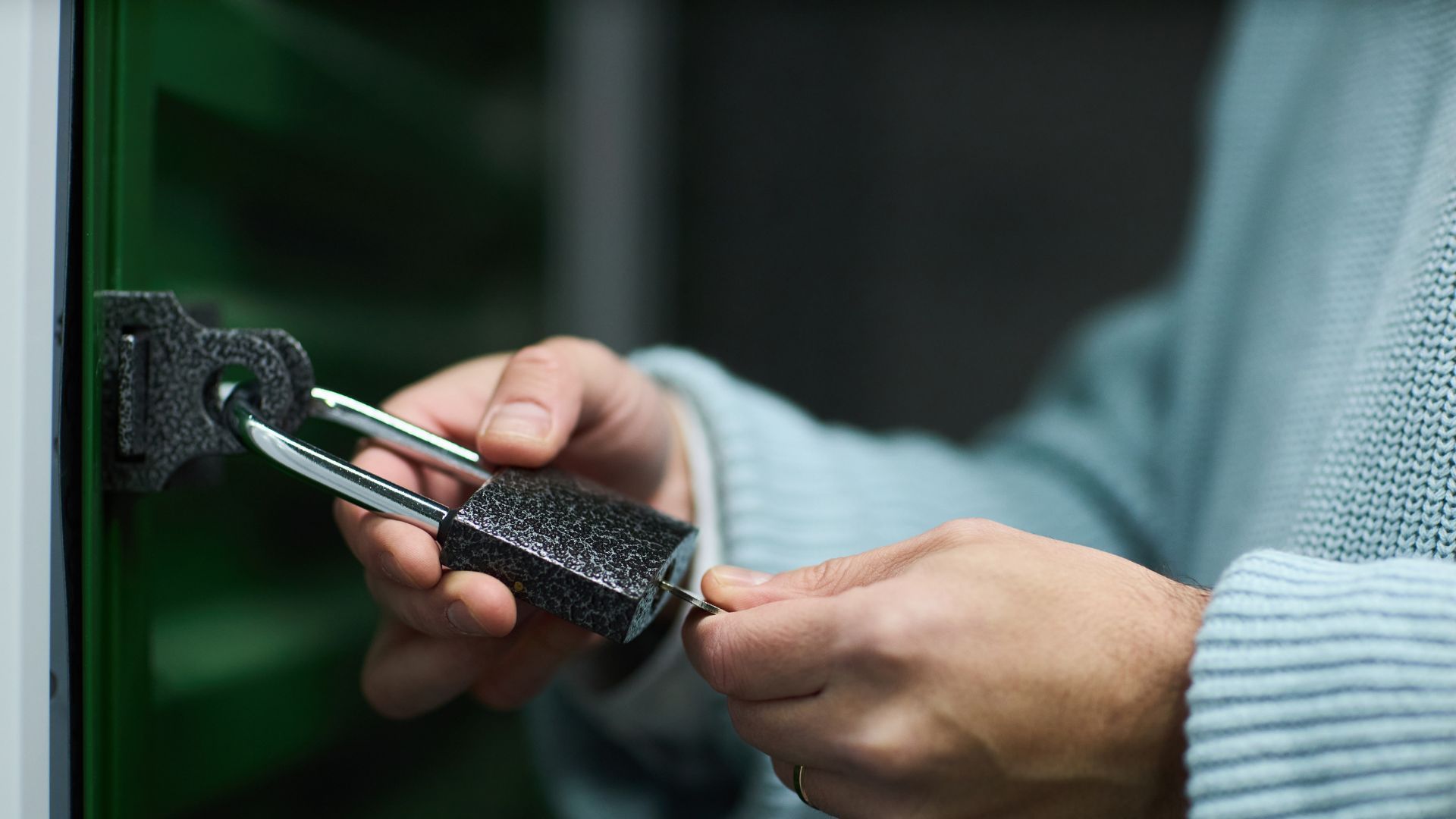 A person wearing a cord jumper using a small key to unlock a padlock.