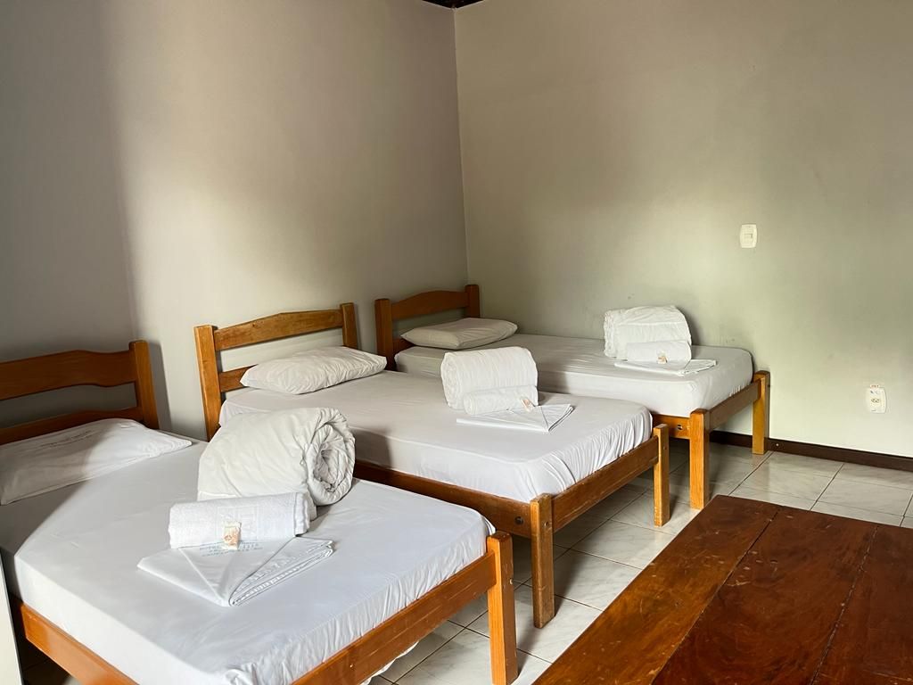 Três camas de solteiro com toalhas brancas dobradas por cima, em um quarto simples com piso de madeira.