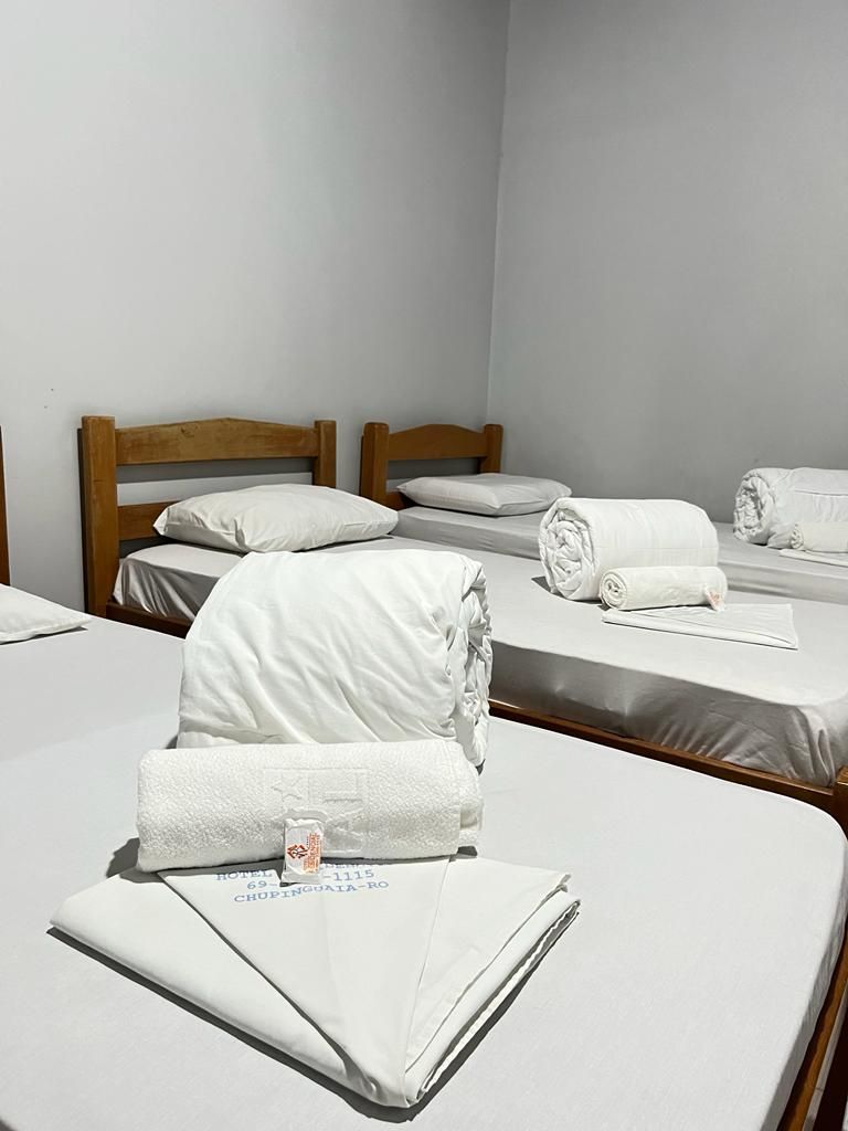 Duas camas de solteiro bem arrumadas com lençóis brancos e toalhas enroladas em um quarto de hóspedes simples em tons de cinza.