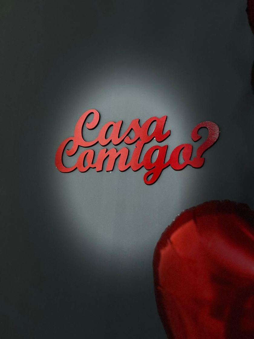 Texto cursivo vermelho com a frase “Casa conmigo?” sobre um fundo escuro, com uma rosa vermelha no canto inferior direito.