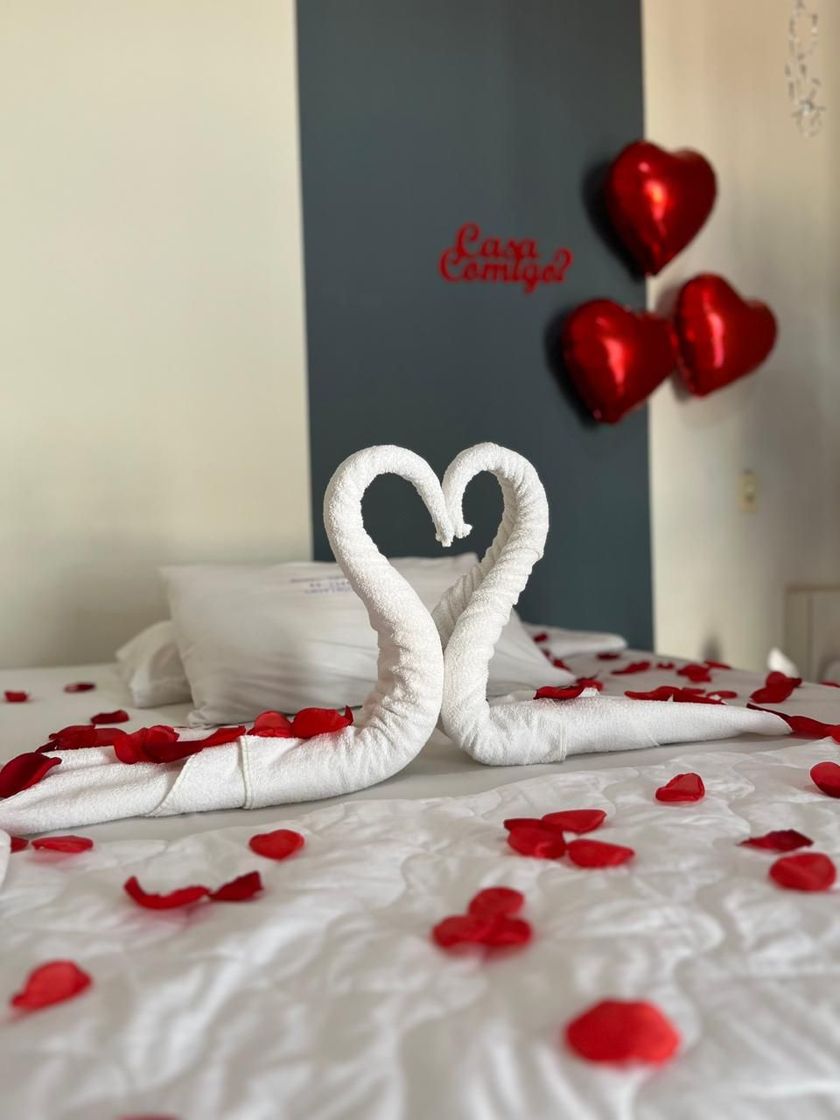 Cisne de toalha em formato de coração sobre uma cama com pétalas de rosa vermelha e balões em formato de coração, decoração romântica.