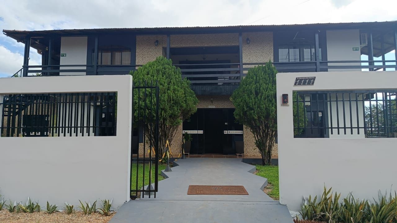 Casa moderna de dois andares com paredes brancas, janelas pretas e uma passarela central emoldurada por vegetação.