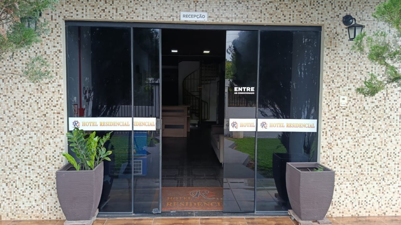 Entrada com fachada de vidro, vasos de plantas e um corredor interno iluminado dentro de um edifício de pedra.