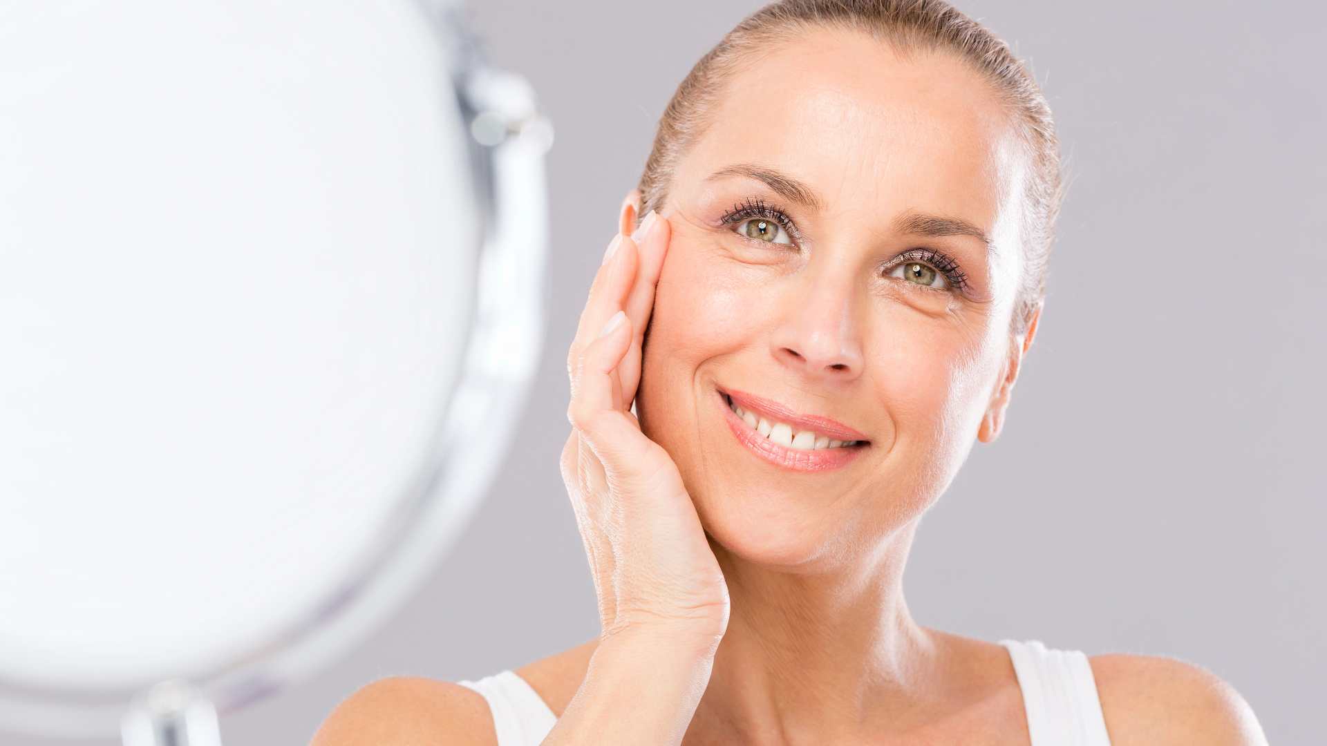 A woman is smiling while looking at her face in a mirror.
