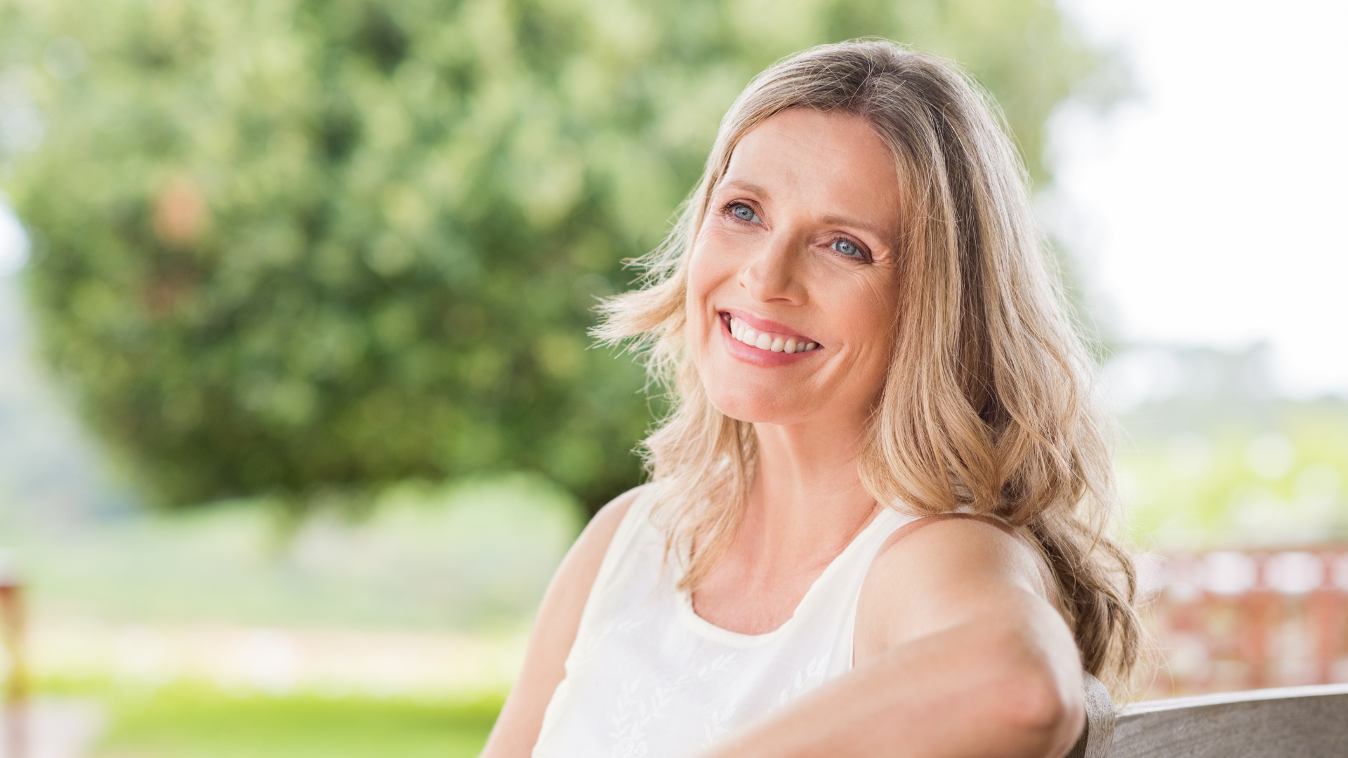 Smiling woman sitting outdoors by a tree in soft natural light