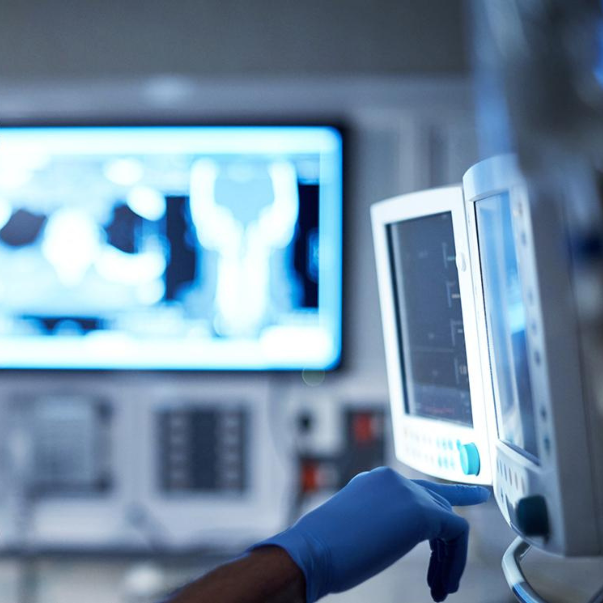 Blue-gloved hand operating a medical monitor in a hospital room