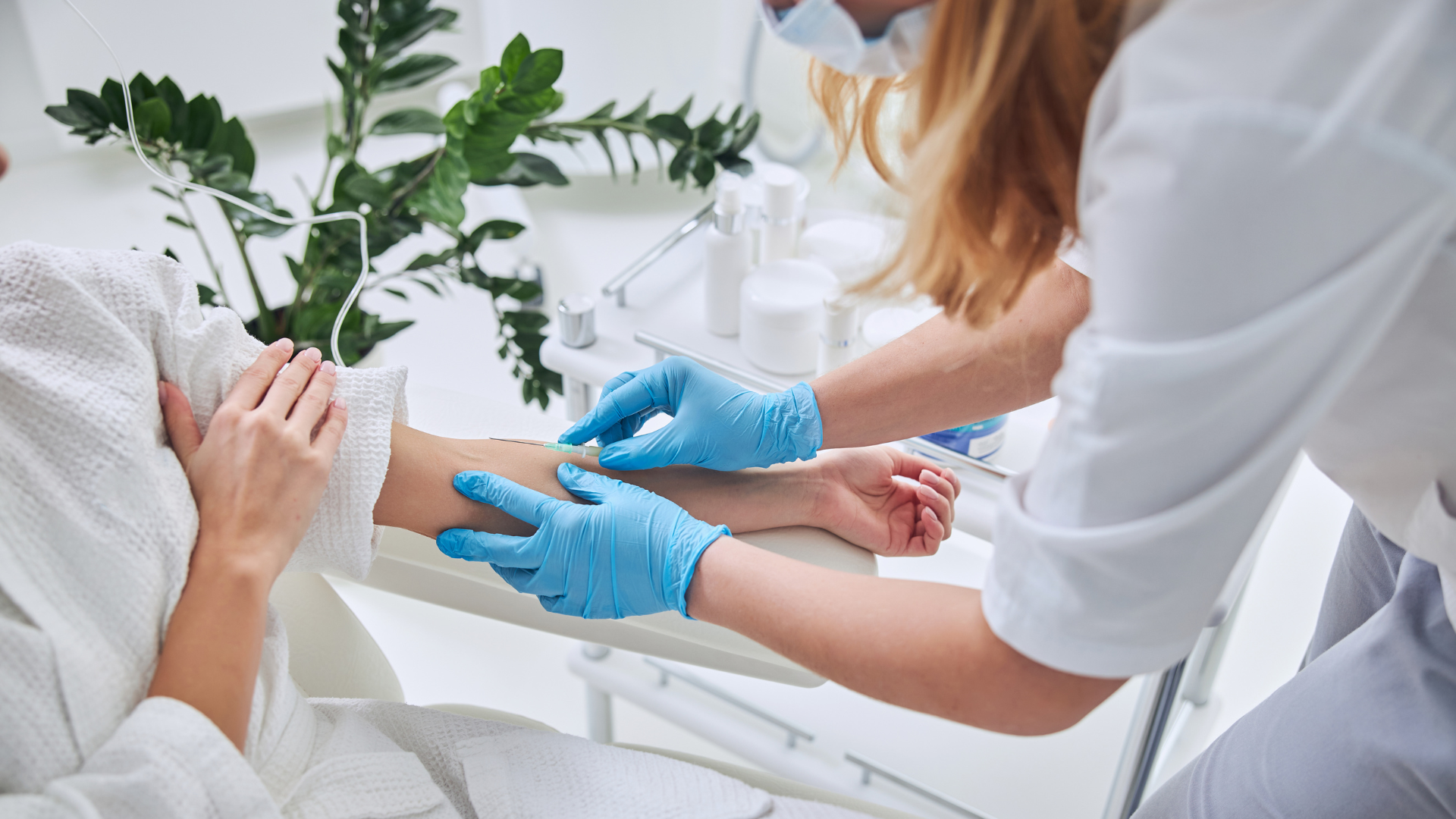 A person in a robe receiving an injection from a healthcare worker wearing gloves and a mask.
