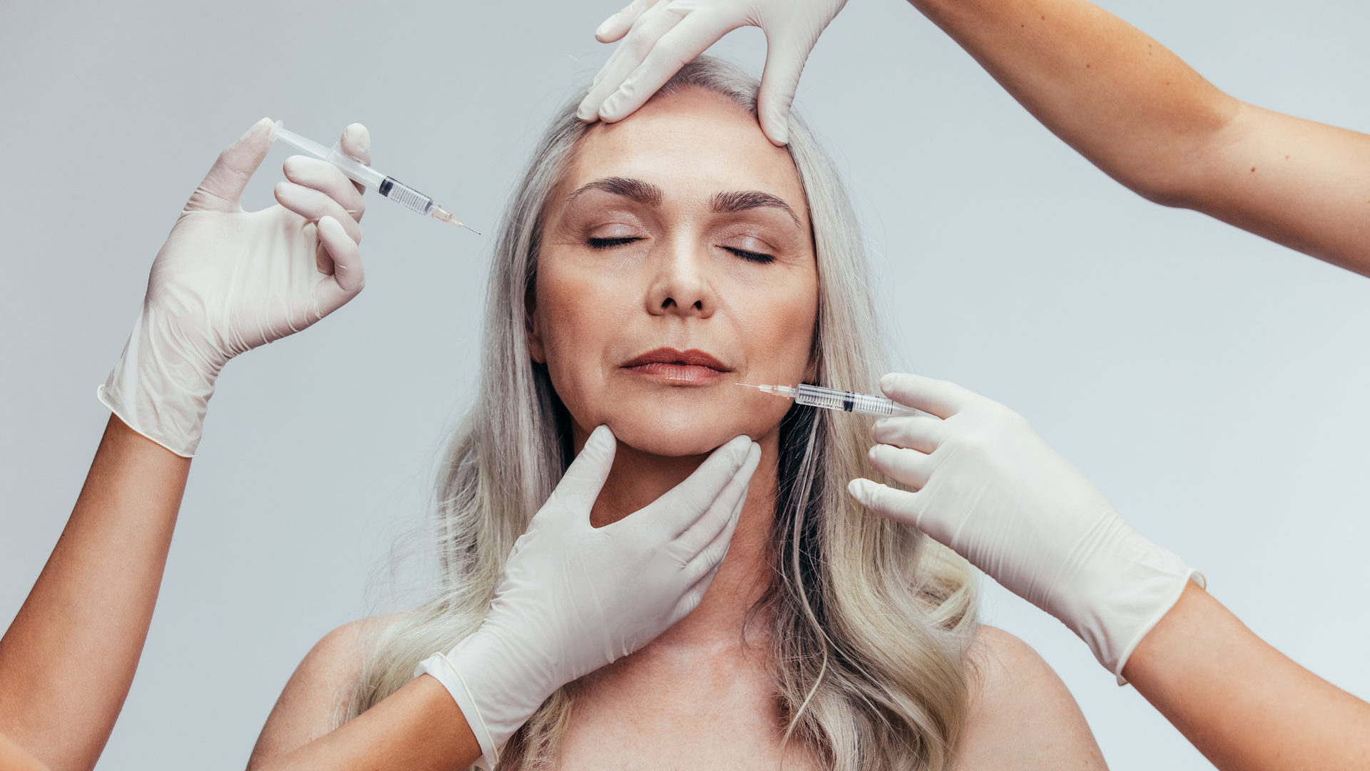 Woman receiving cosmetic injections from multiple hands.