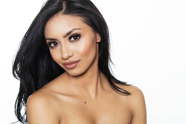 Woman with dark hair looking at the camera, wearing makeup. White background.
