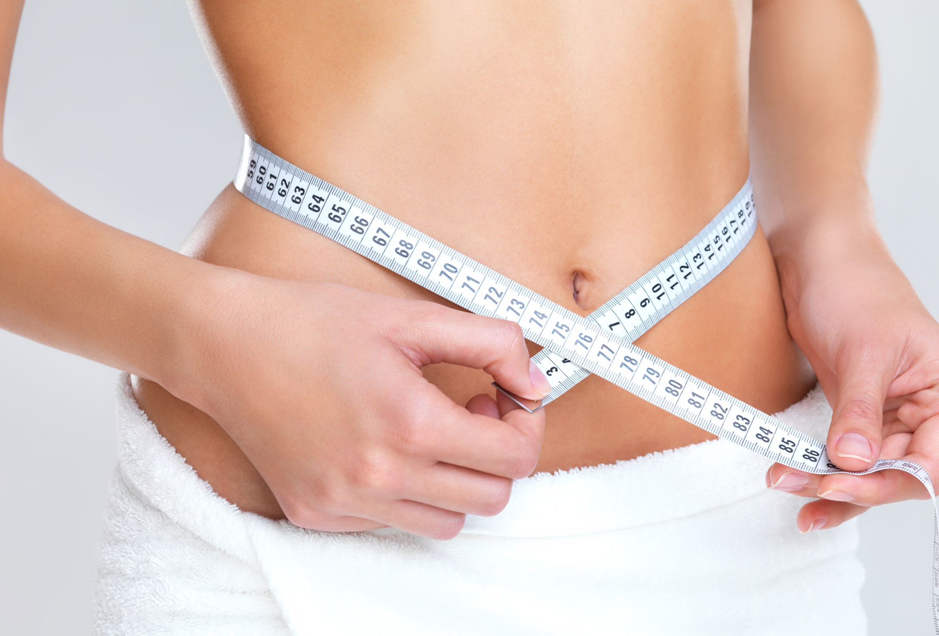 A woman is measuring her waist with a tape measure.