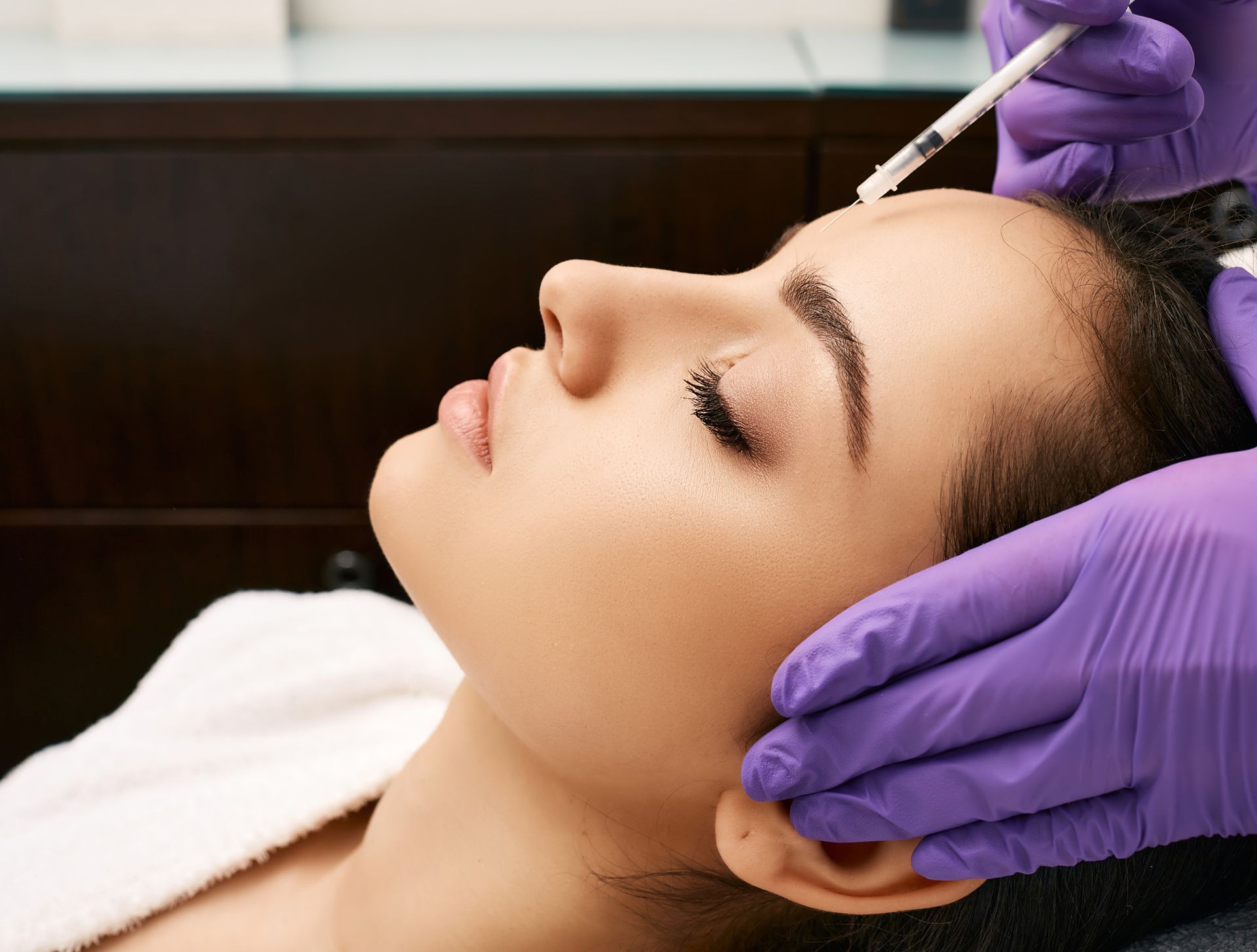 A woman is getting a botox injection in her forehead.