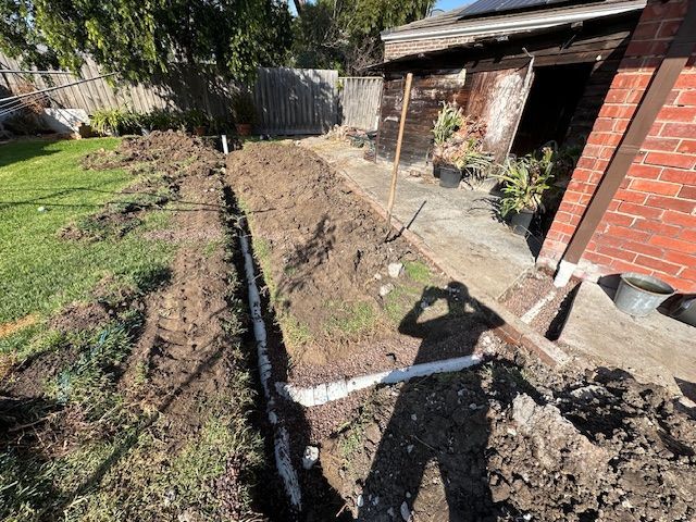 Trench with white pipes in a backyard. Man's shadow visible — Mezcon Renovations & Maintenance in Heidelberg, VIC