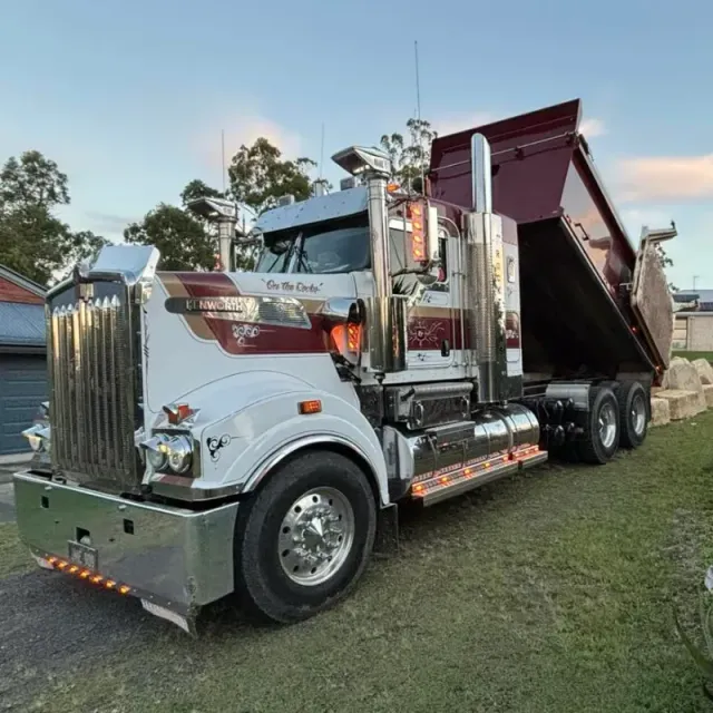 A large sandstone dump truck is parked in a grassy area next to a house.