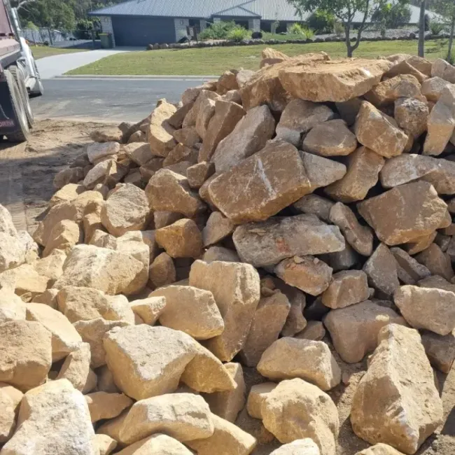 A pile of sandstone rocks is sitting in the dirt in front of a house.