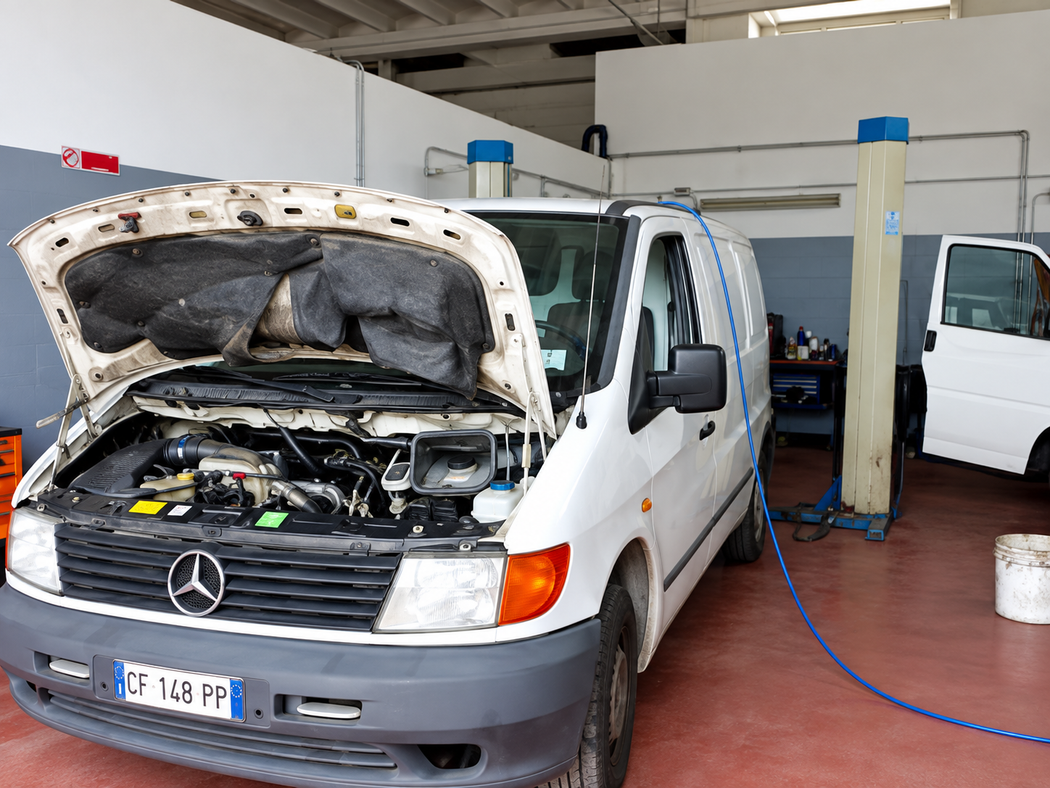 Furgone bianco con il cofano aperto in un’officina, collegato ad apparecchiature di servizio sul pavimento.