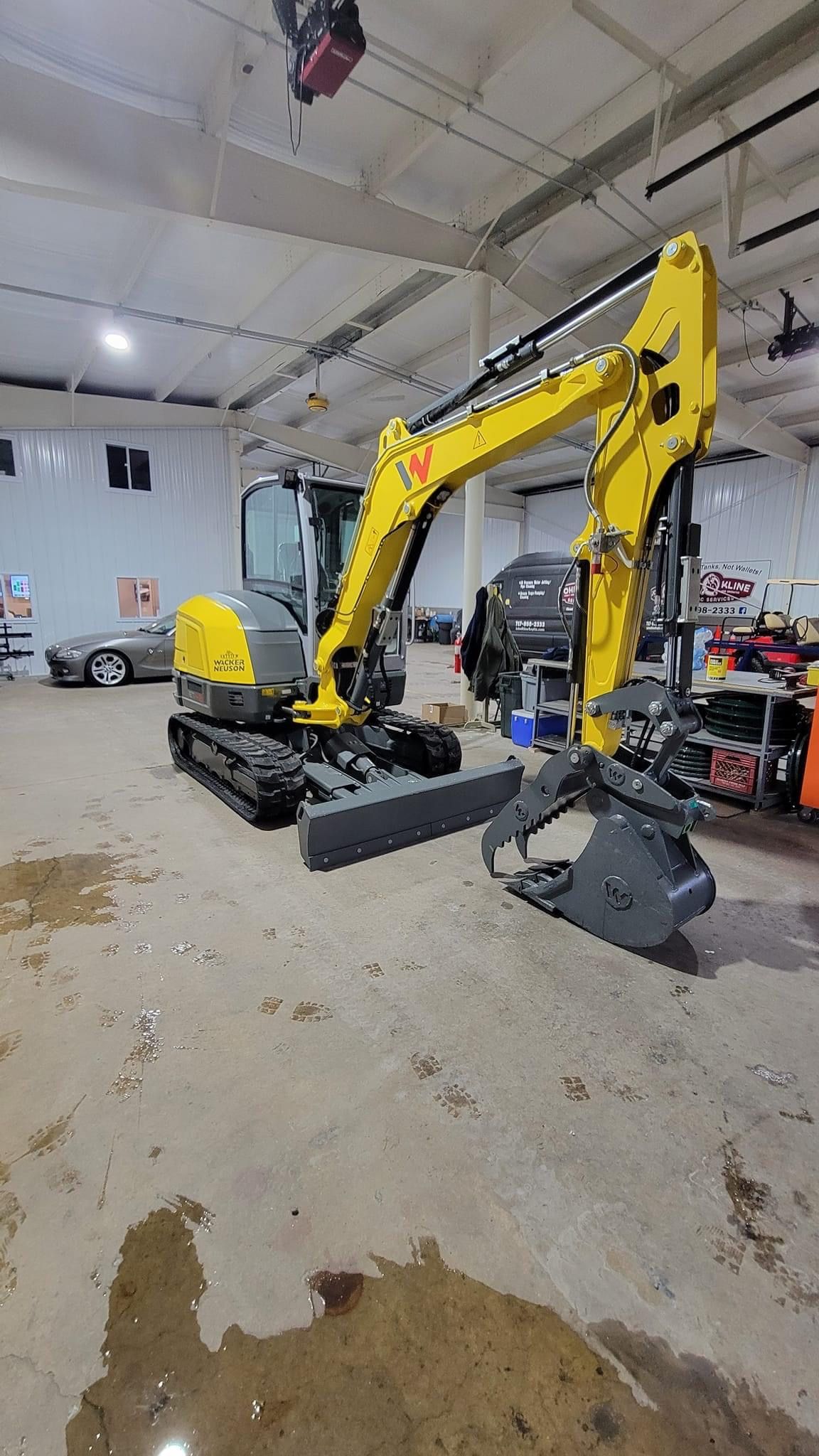 A yellow excavator is parked in a garage next to a car.