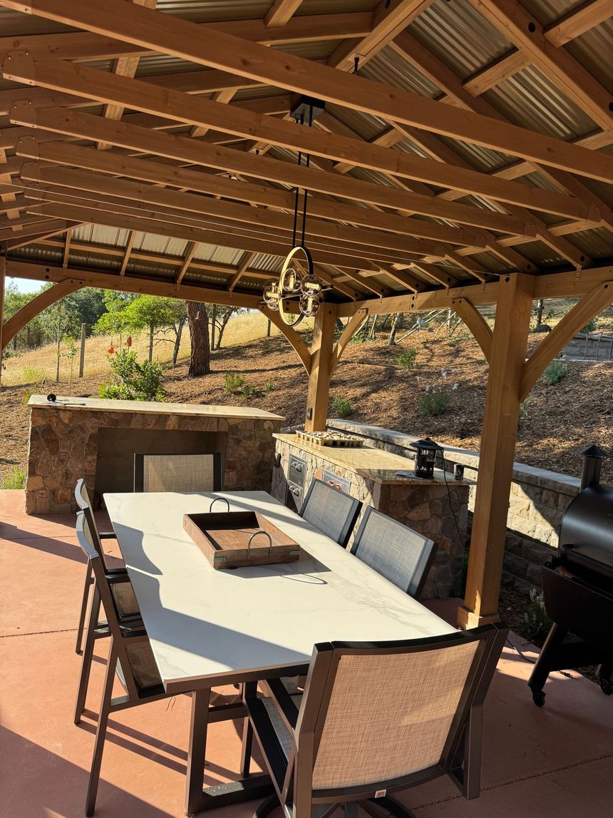 Outdoor patio dining area under a wooden pergola with a long table and cushioned chairs