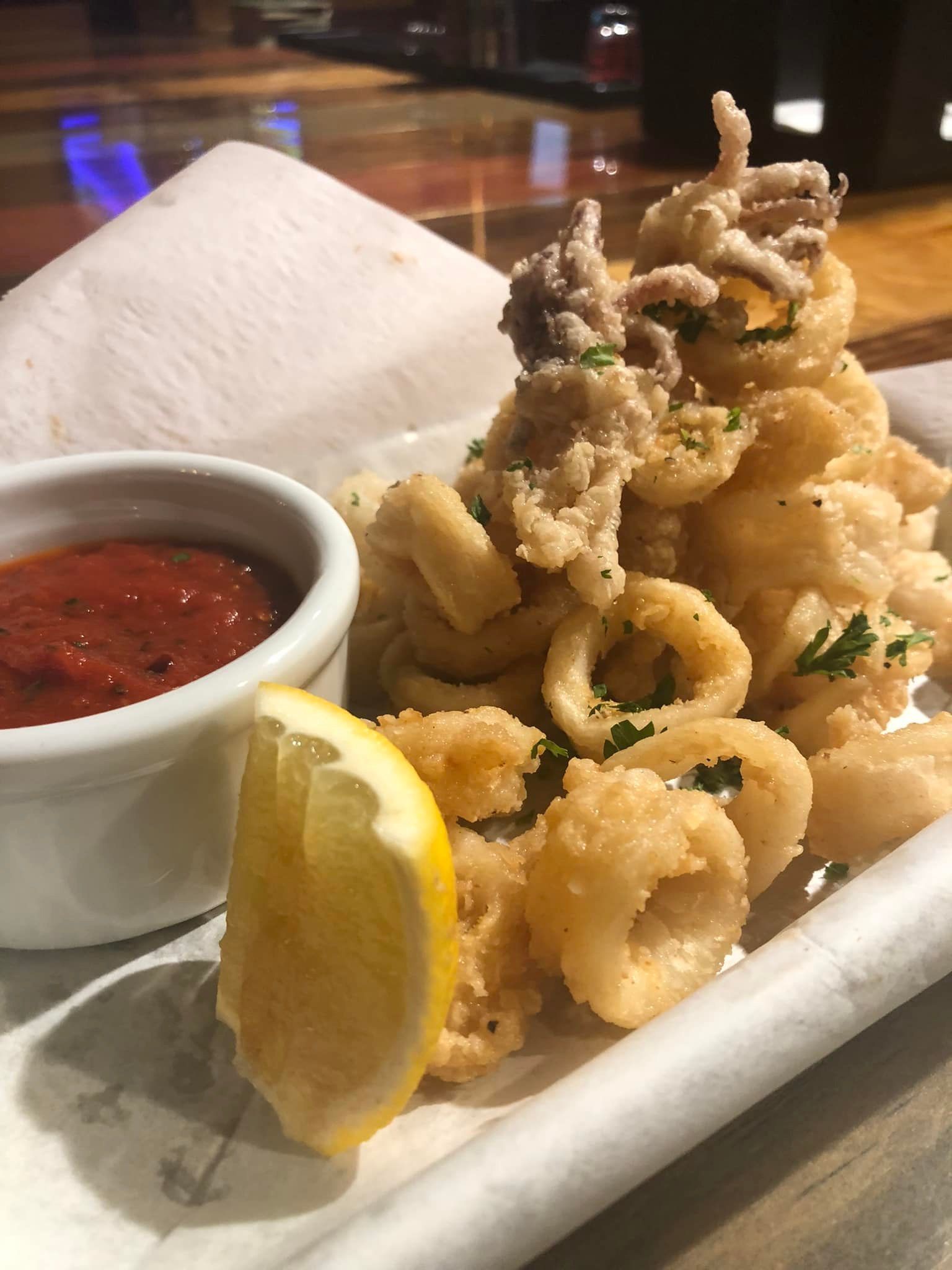 Fried calamari with marinara sauce and a lemon wedge.