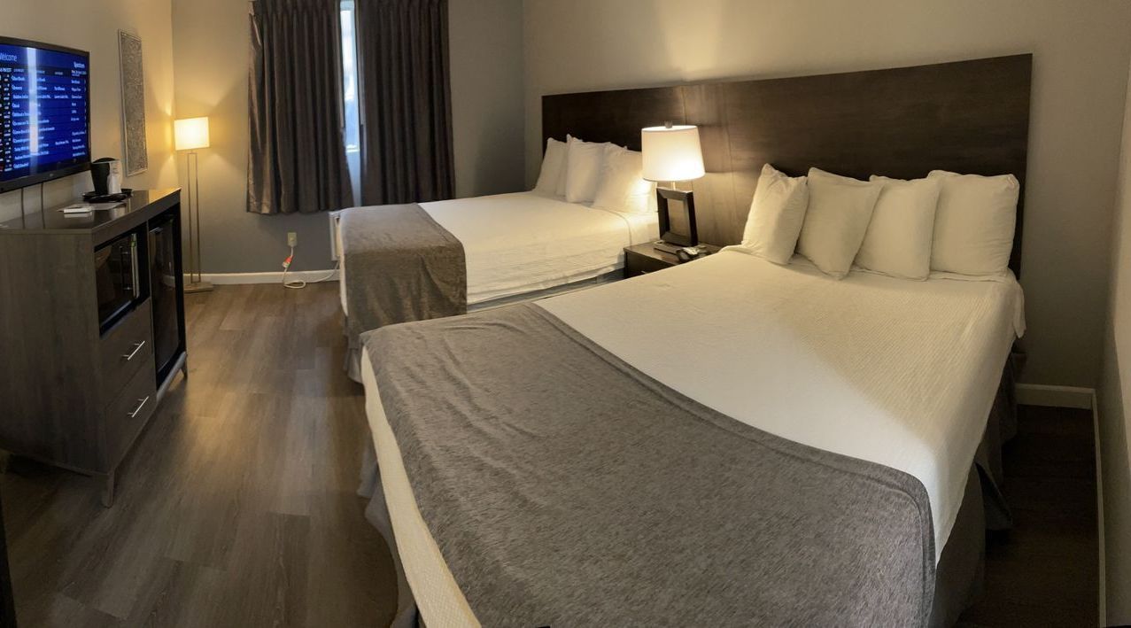 Hotel room with two queen beds, lamps, TV, and gray accents.