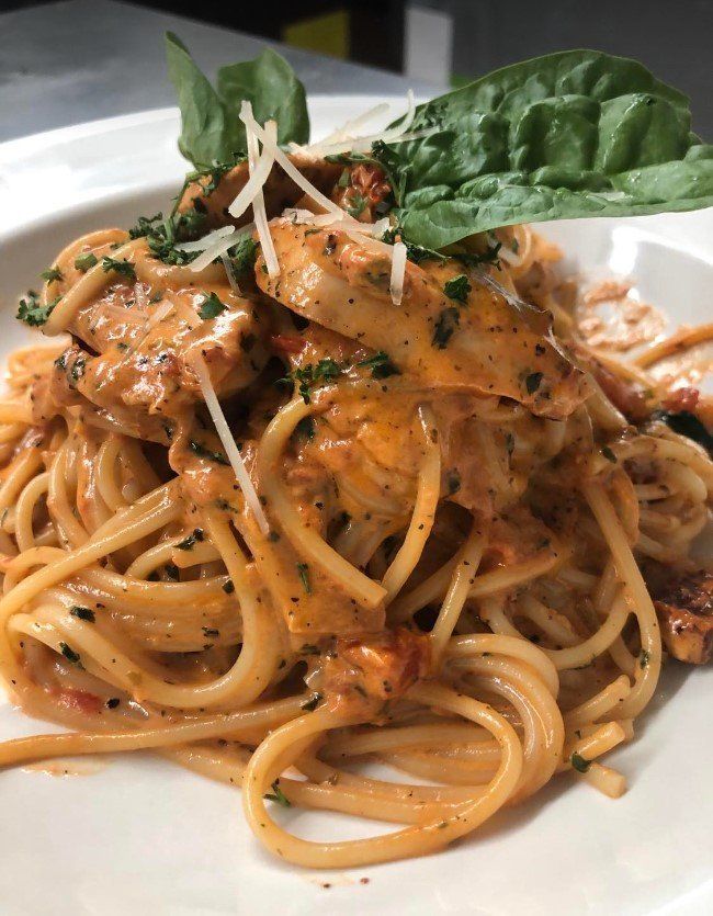 Spaghetti with creamy tomato sauce, chicken, basil, and cheese on a white plate.