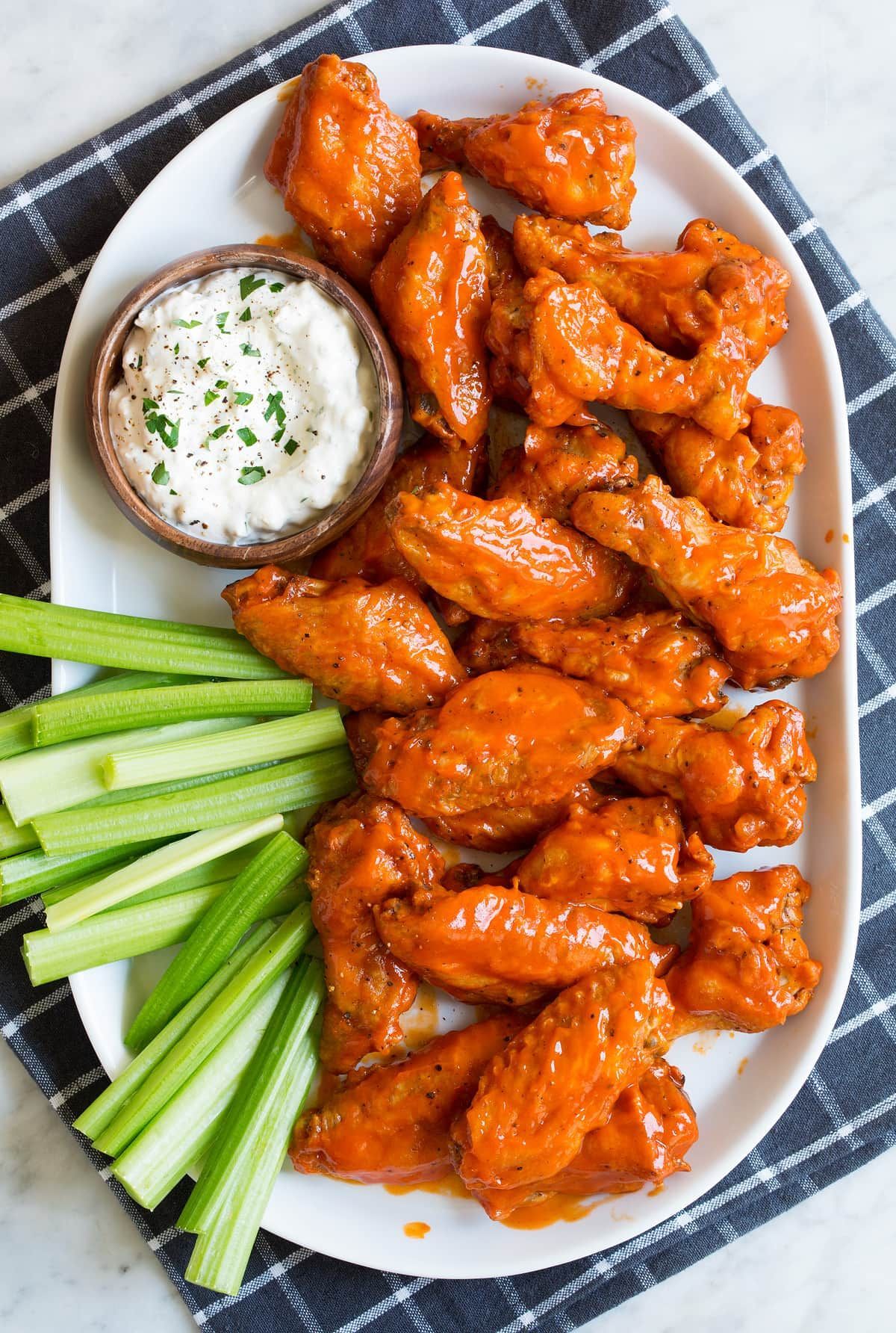 Buffalo wings with blue cheese dip and celery sticks on a white platter.