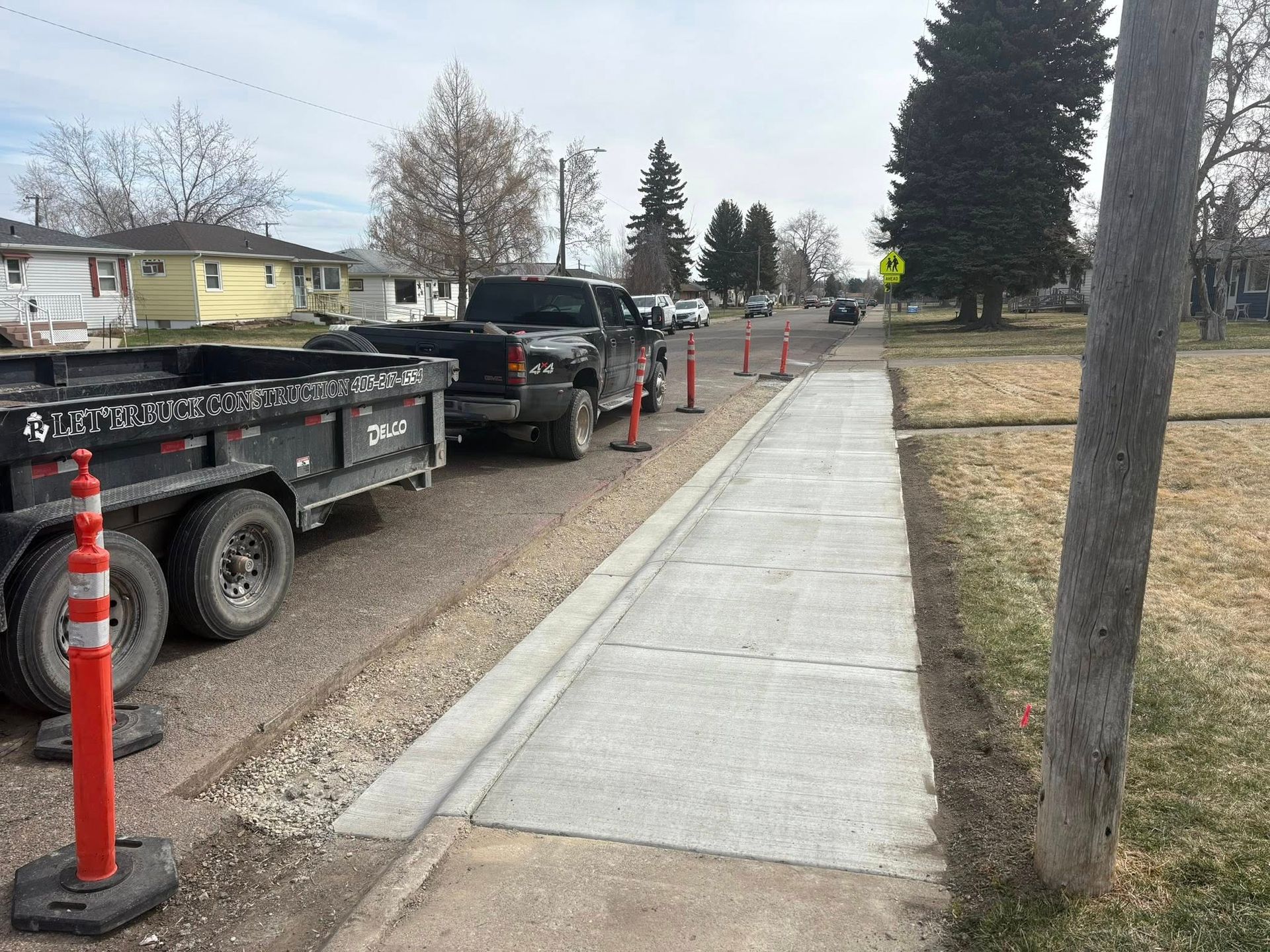 Sidewalk beside parked work trucks, marked by orange cones along a residential street.