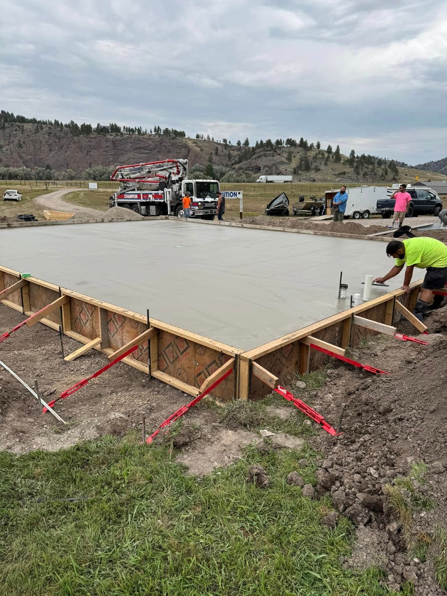 Concrete slab being poured at a construction site, with workers and a pump truck nearby.