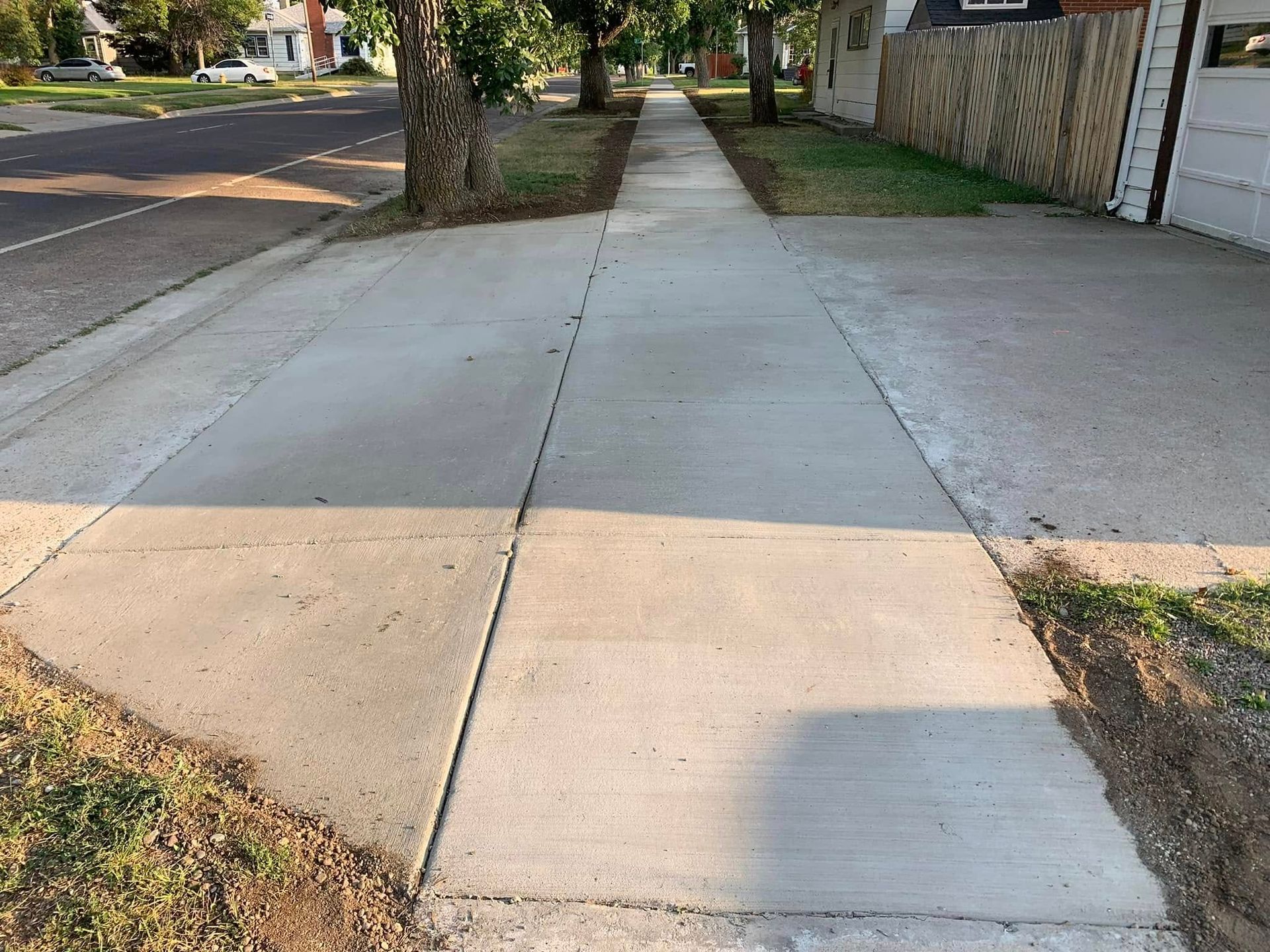 Empty concrete sidewalk beside a street, with trees and a driveway along the right side.