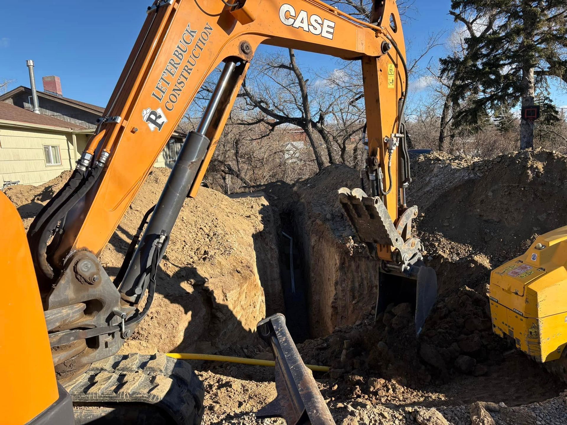 Orange CASE excavator digging a trench beside a yellow machine in a dirt work site