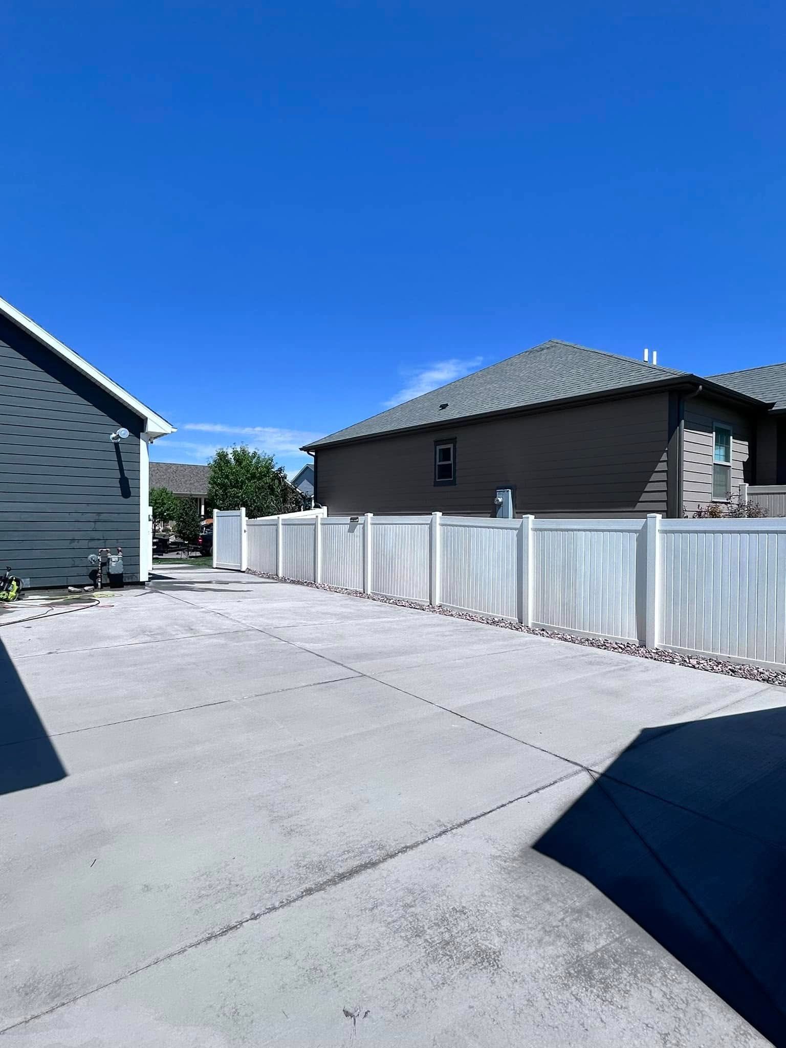 Sunny driveway between houses with a white fence and blue sky