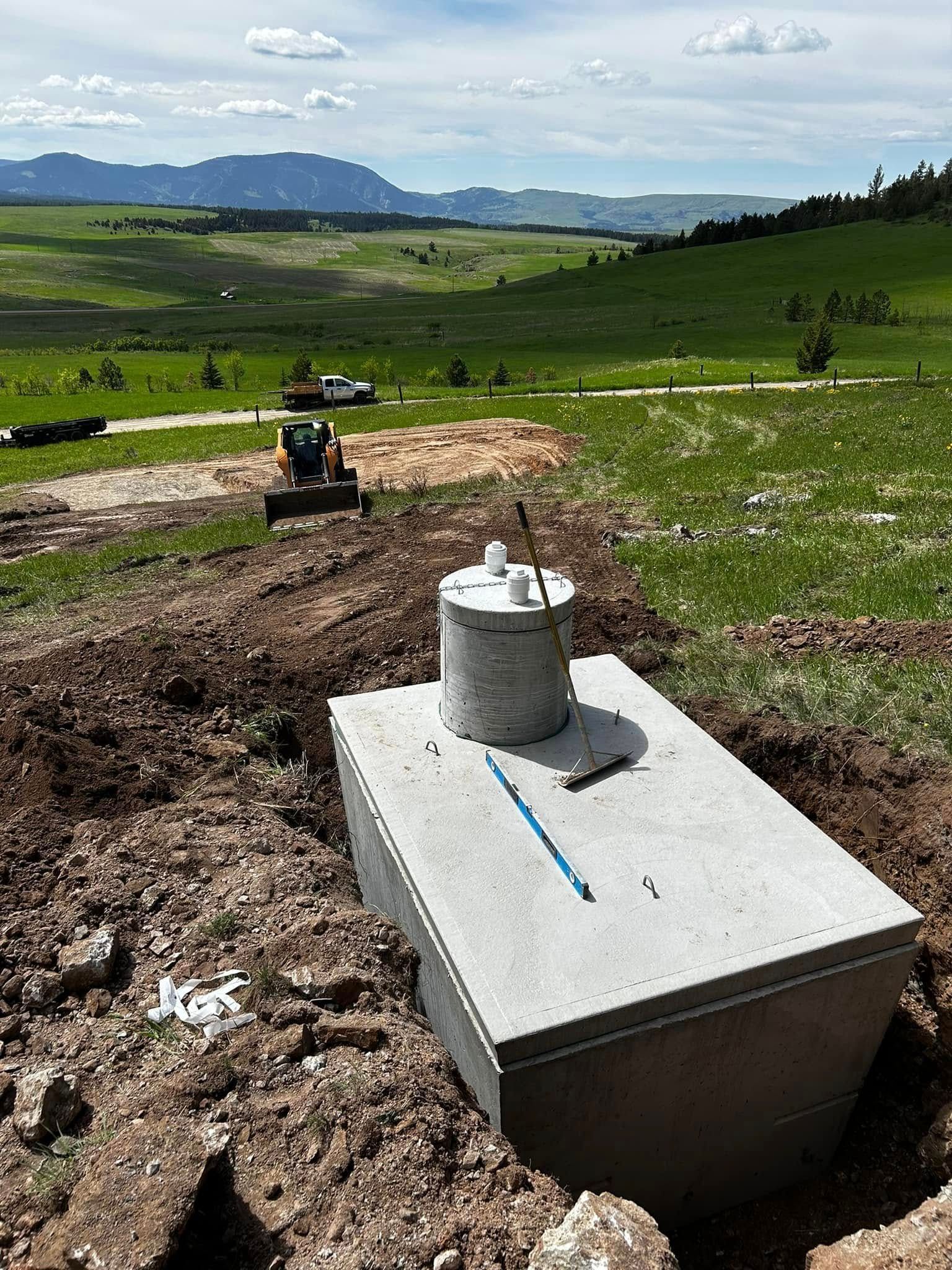 Concrete utility box in a muddy field, with a grassy landscape and mountains in the background.