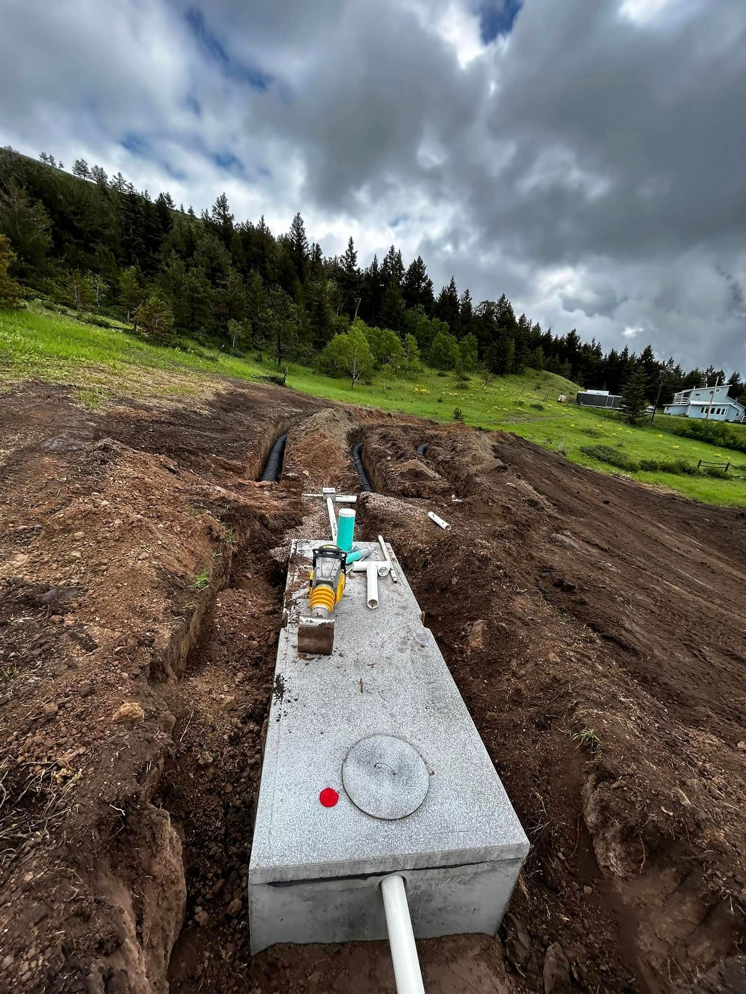 Gray concrete utility box in muddy field with pipes and fittings under cloudy sky