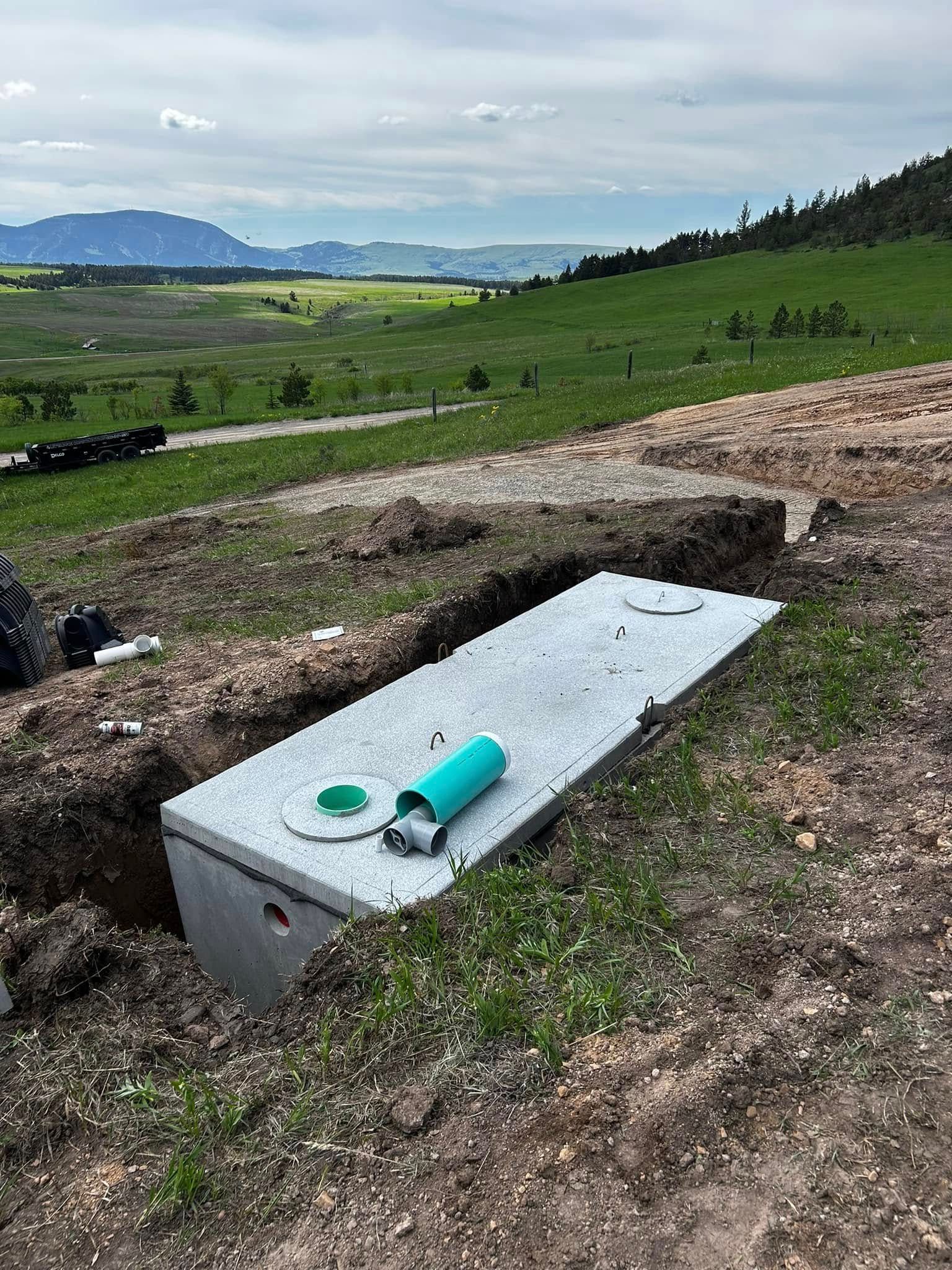Concrete utility box with green pipe lying on a grassy hillside, overlooking a distant valley and lake