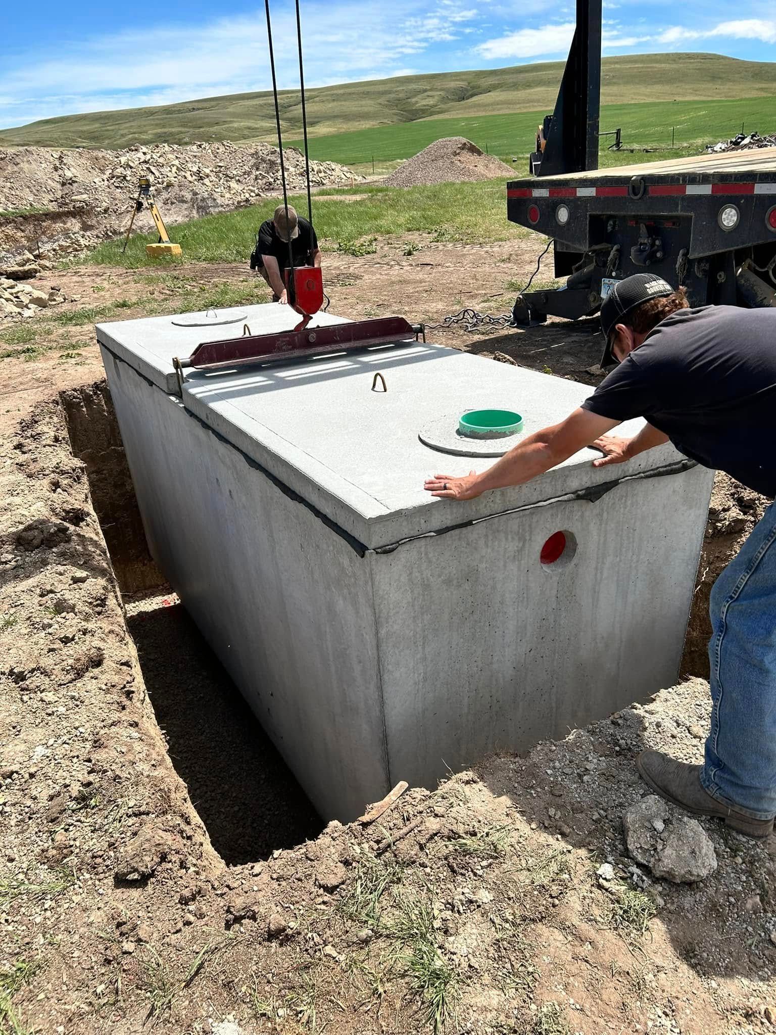 Worker using a crane to place a concrete utility vault cover at a construction site