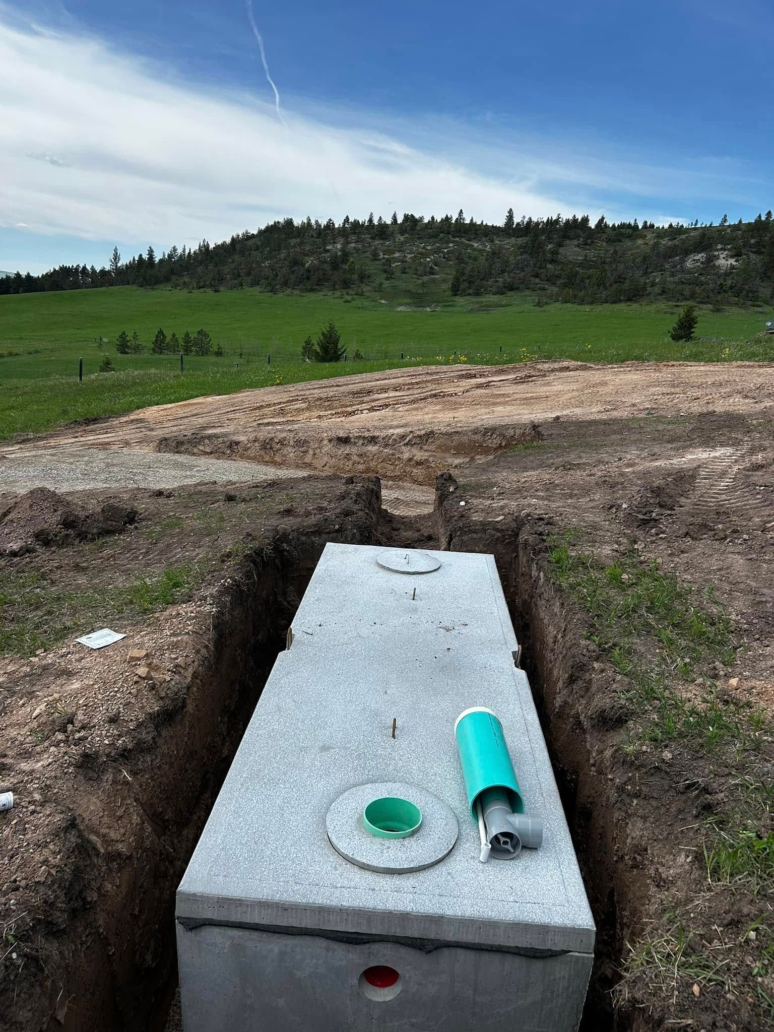 Concrete utility box in a grassy field with an open pipe and green cap under a cloudy sky