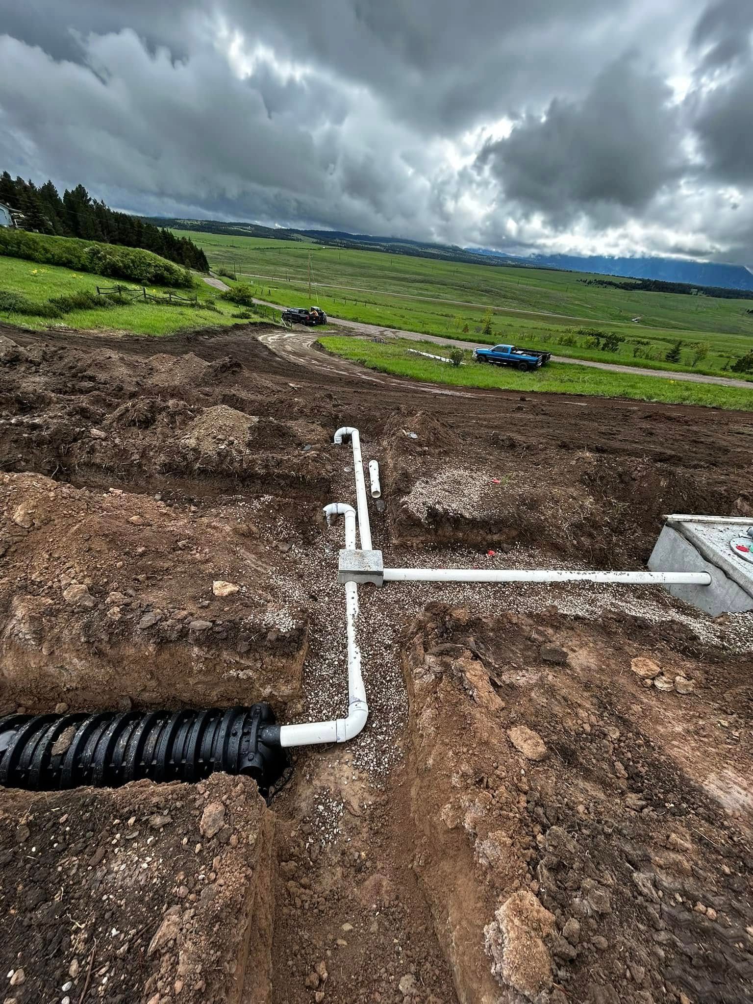 Construction trench with white drainage pipes in a muddy field under dark cloudy skies