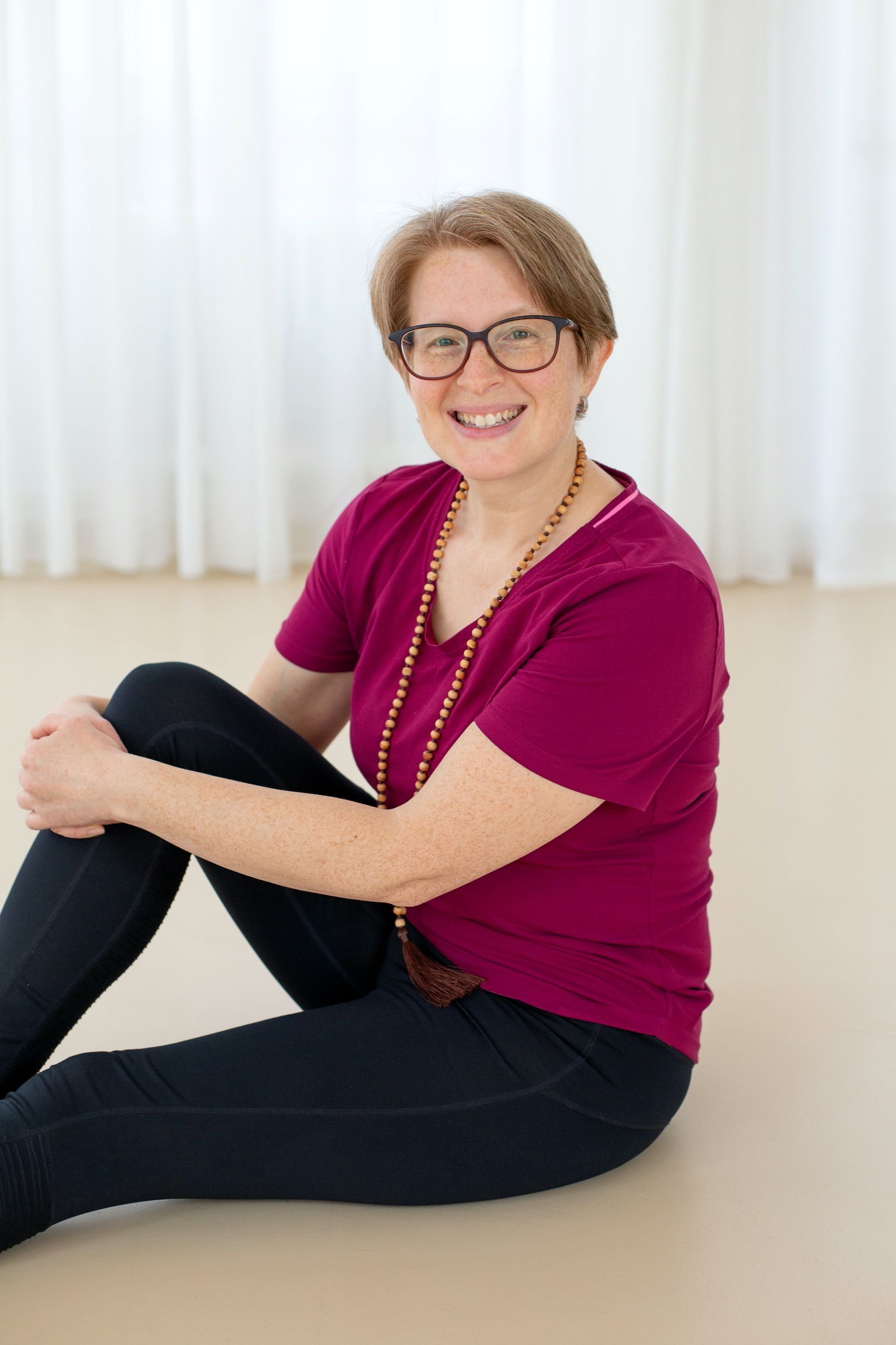 Eine Frau mit Brille und lila Hemd sitzt auf dem Boden.