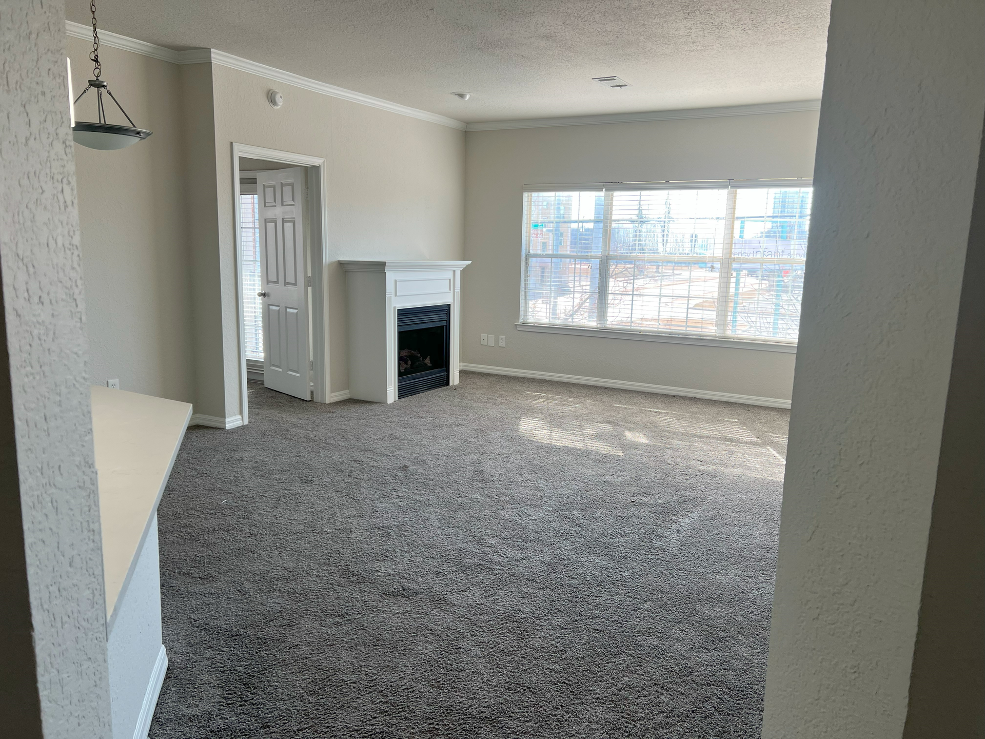 Empty carpeted living room with large window and fireplace, viewed from a doorway