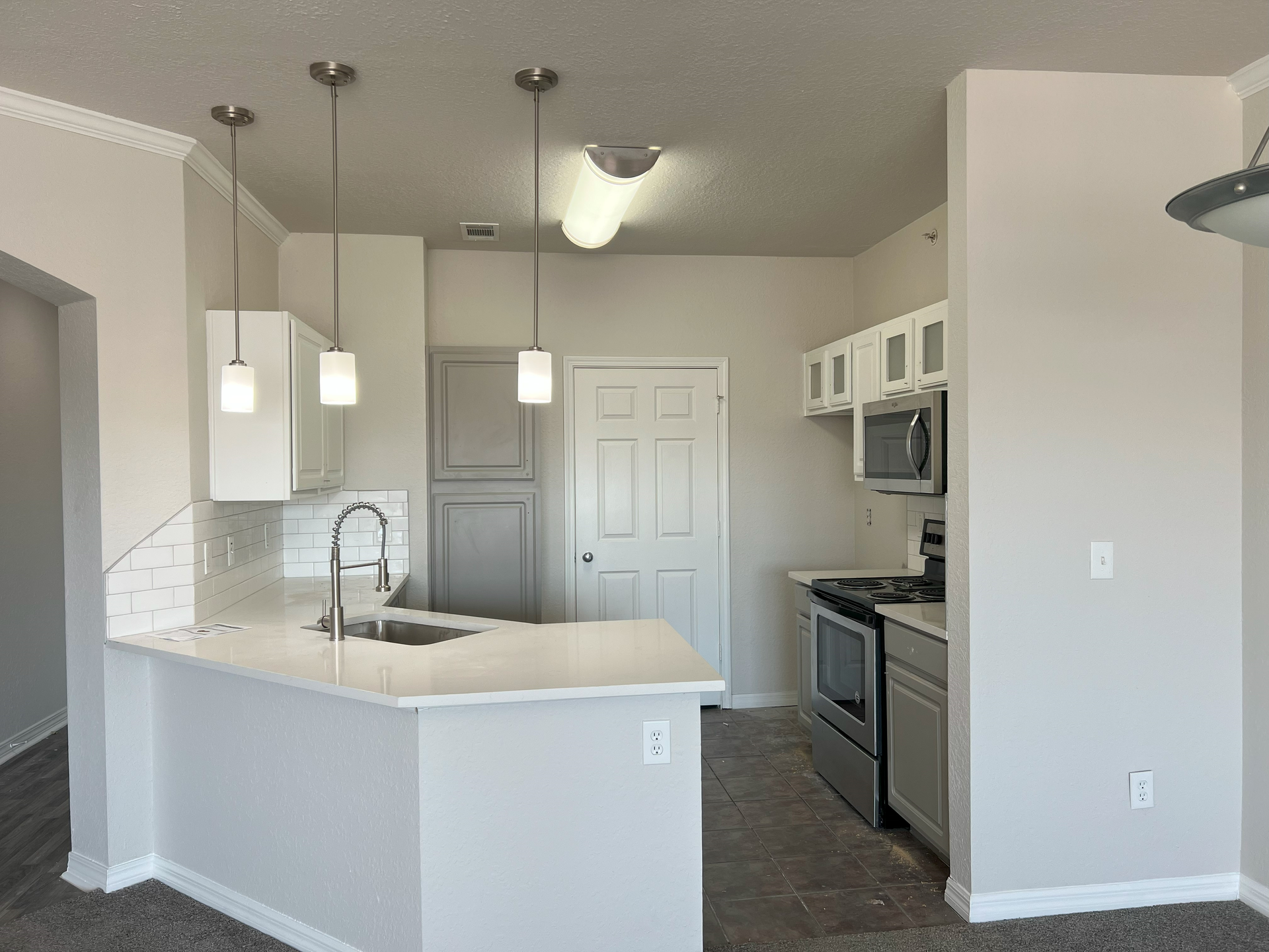 Bright kitchen with white cabinets, gray walls, pendant lights, and a curved breakfast bar.