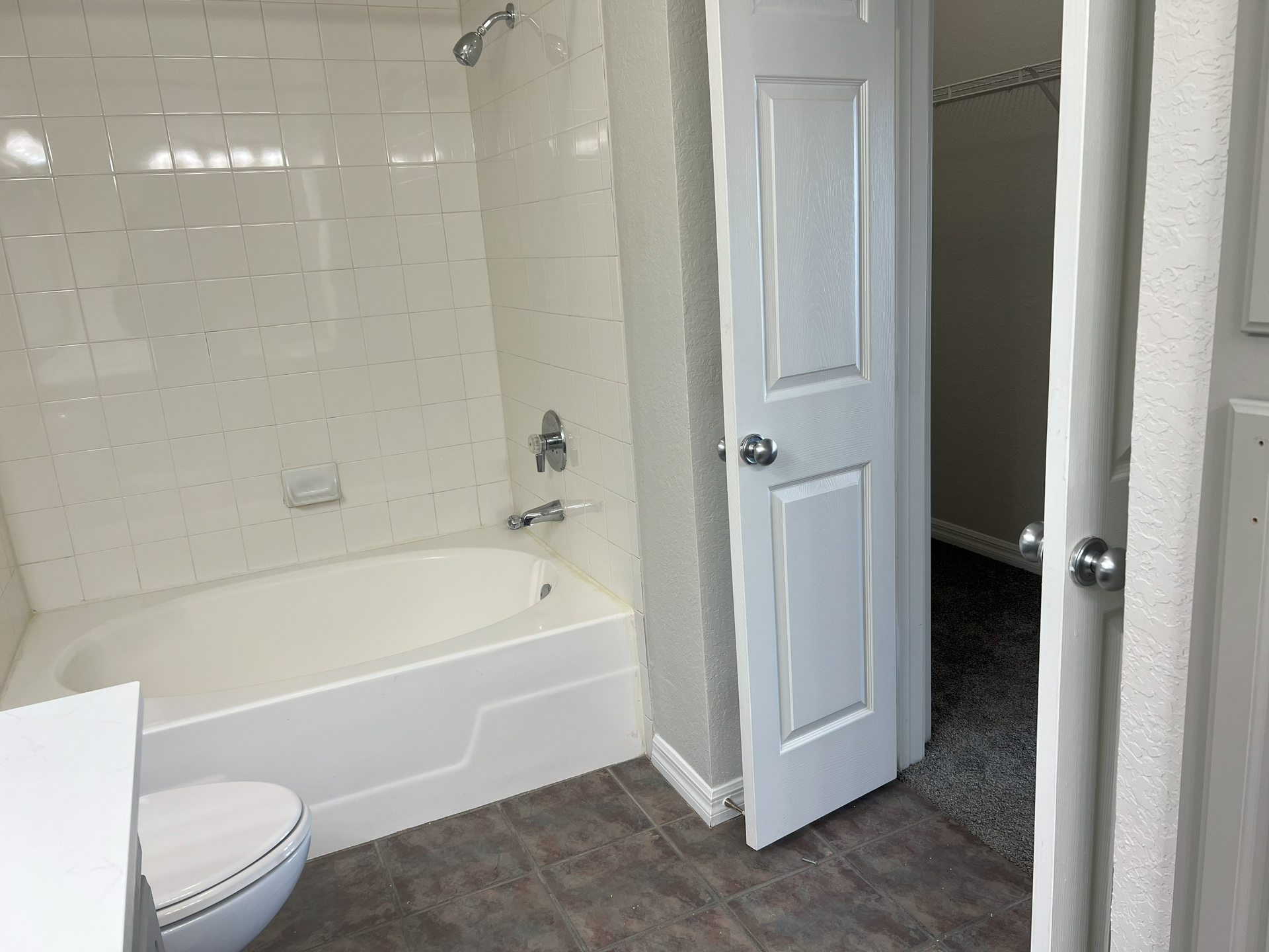 Small white bathroom with tub-shower, toilet, and open door to a carpeted hallway.