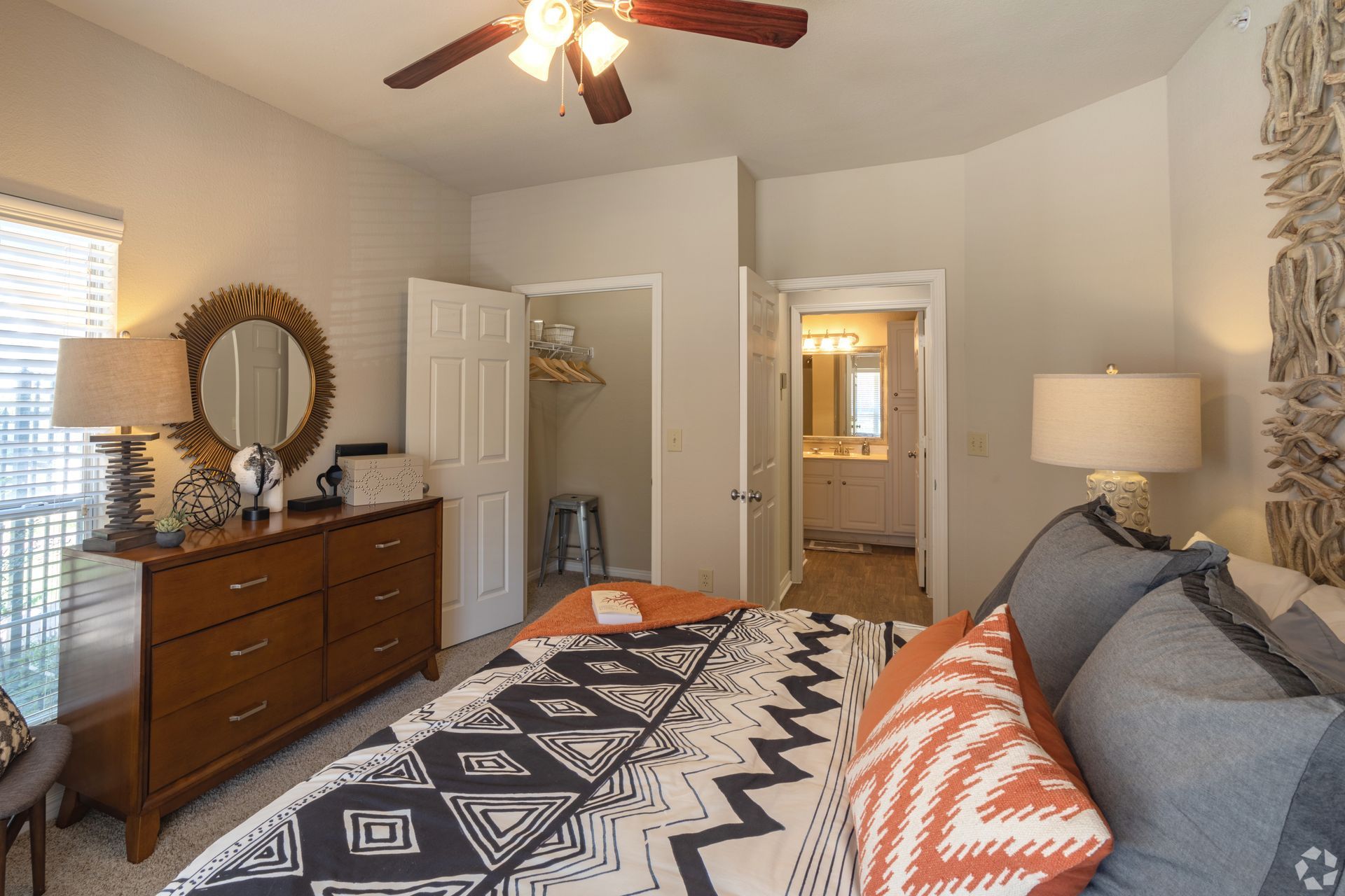 Bedroom with a gray bed, orange pillows, dresser, and ceiling fan in a neutral-toned home