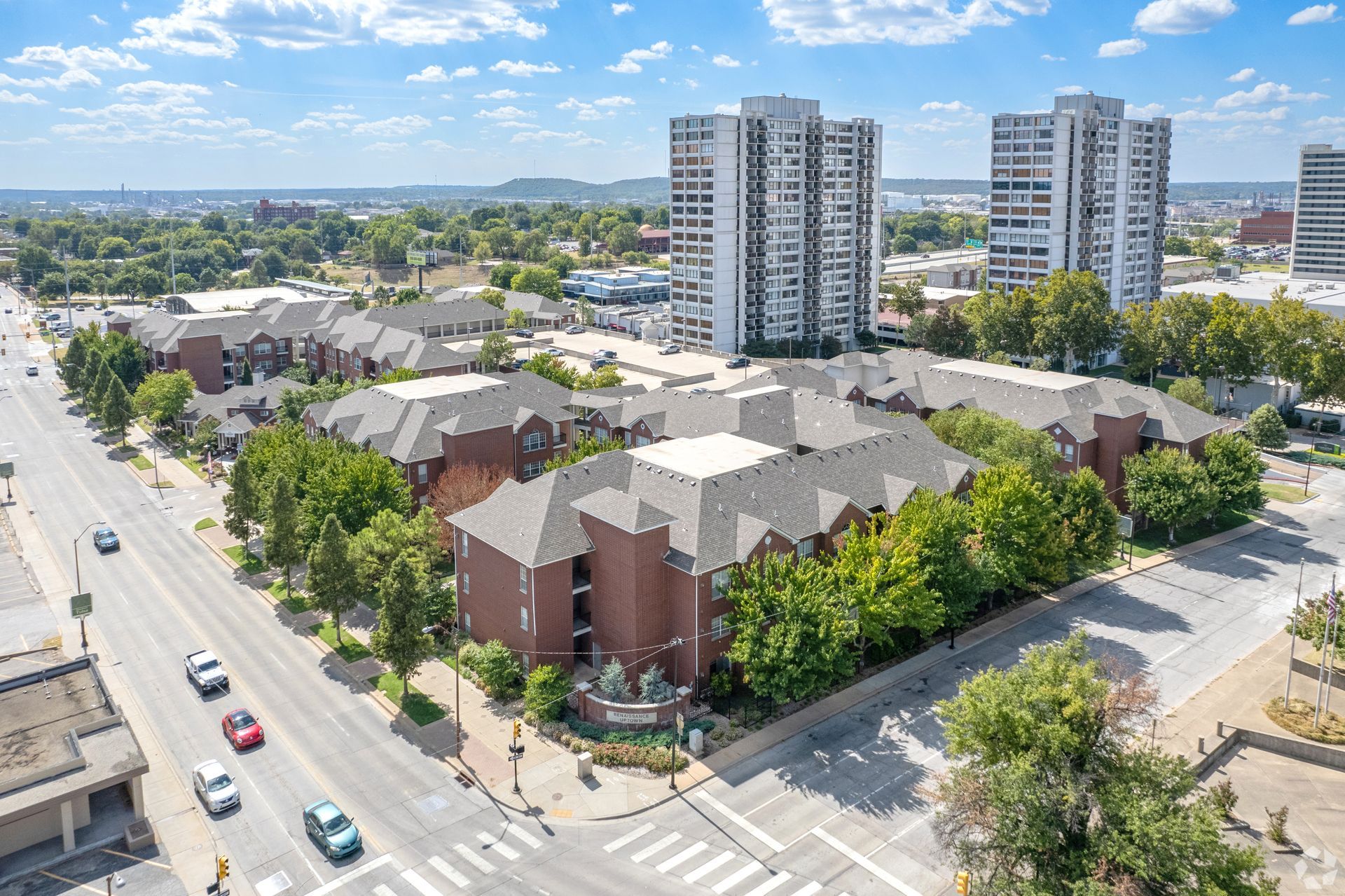 Aerial view of a residential complex with brick buildings, tree-lined streets, and tall apartment towers nearby